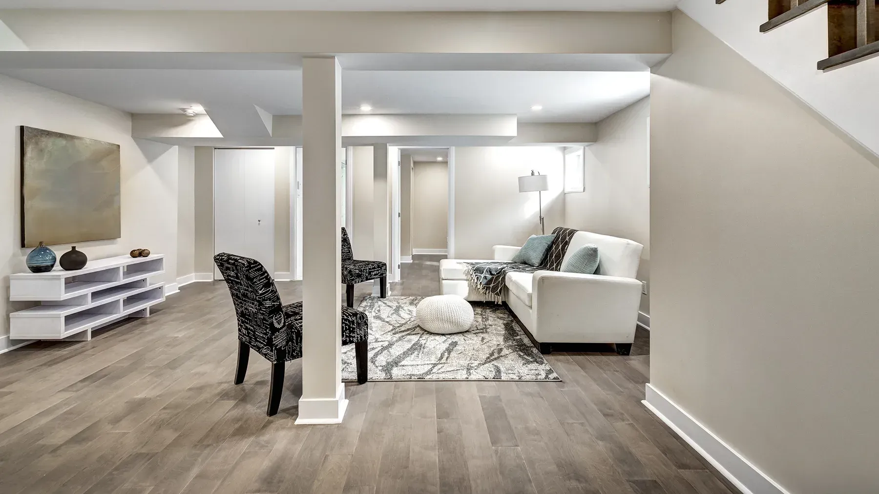 Finished basement with wood flooring, white walls, modern furniture, and a rug.