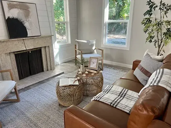 Living room with brown leather sofa, rug, and fireplace. Two windows provide natural light.