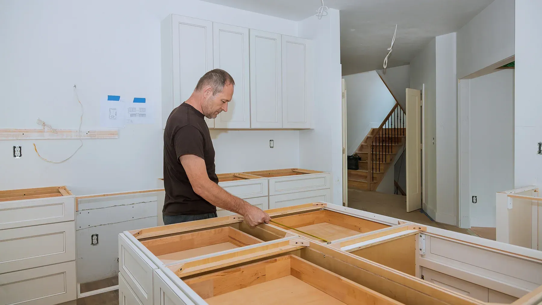 Man installing kitchen cabinets in a room under construction.