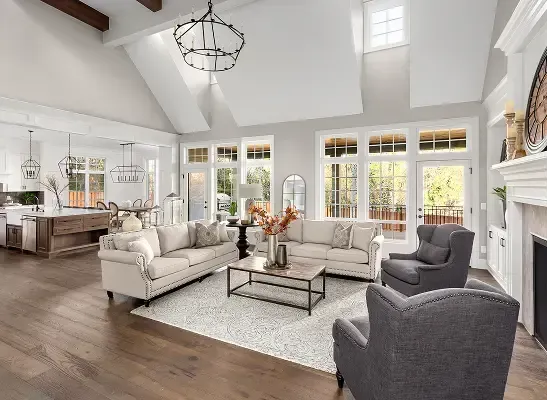 Couple takes a break while painting a room, surrounded by supplies and boxes. Bright open living room with white sofas, gray chairs, fireplace, and large windows.