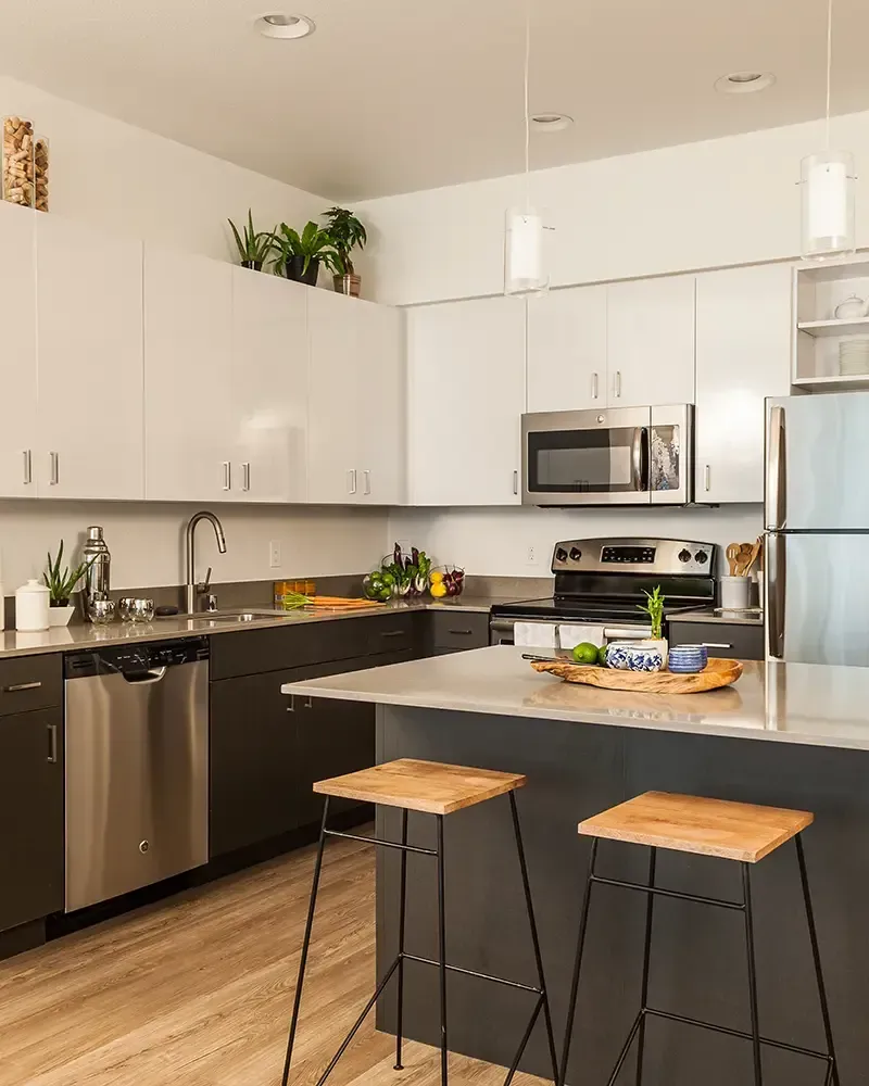 Modern kitchen with white cabinets, black countertops, stainless appliances, and two stools at the island