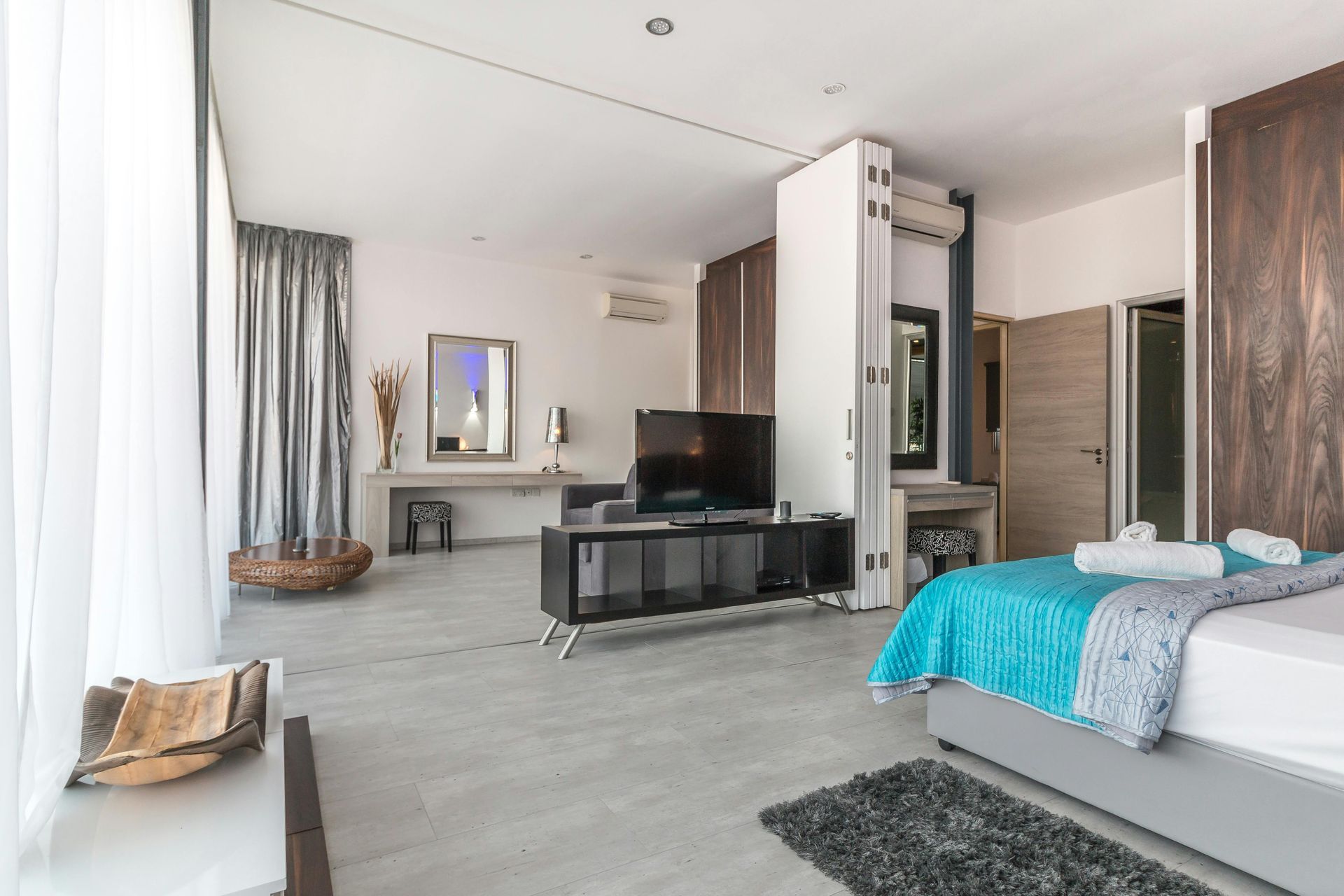Modern bedroom with a bed, TV, desk, and large window in a bright, minimalist interior