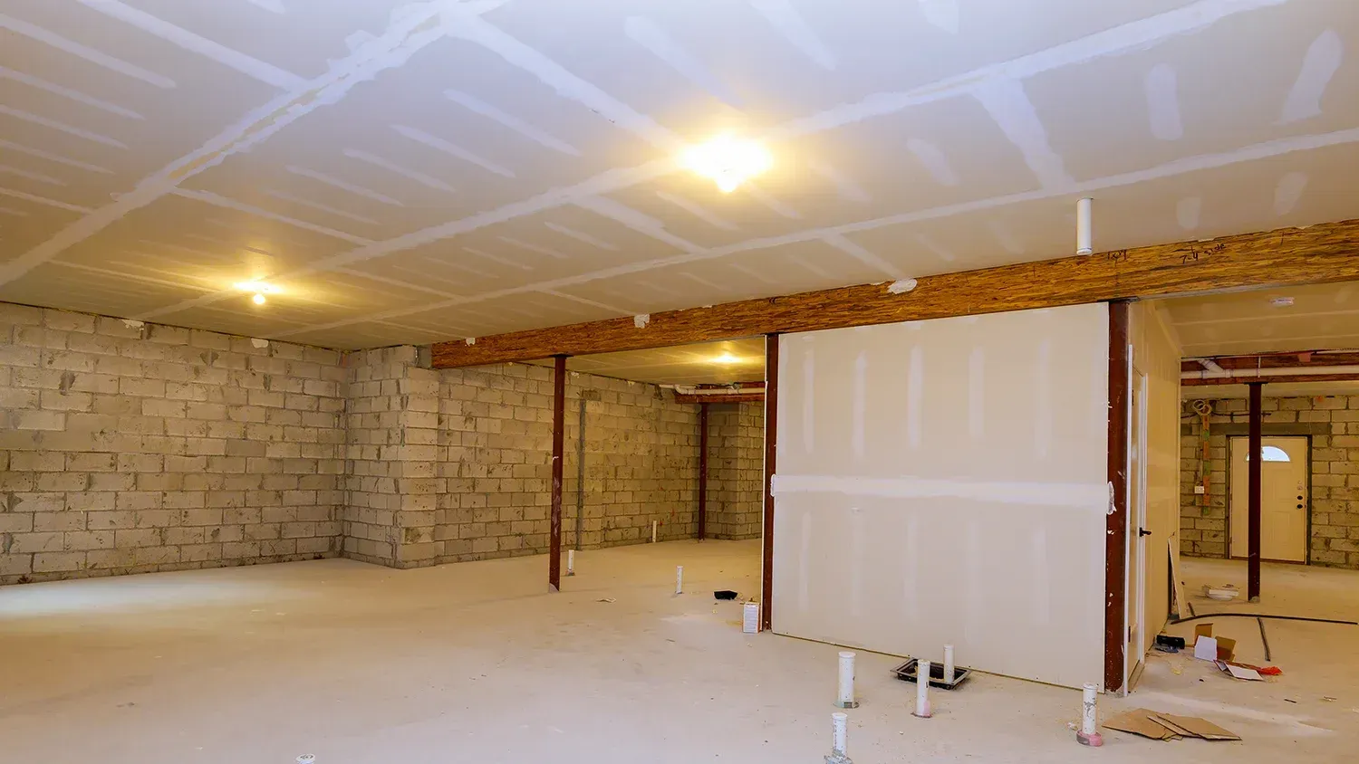 Unfinished basement with exposed brick walls, drywall, support beams, and recessed lighting.