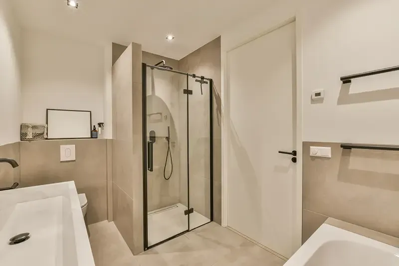 Modern beige bathroom with a glass walk-in shower, sink, toilet, and towel bar