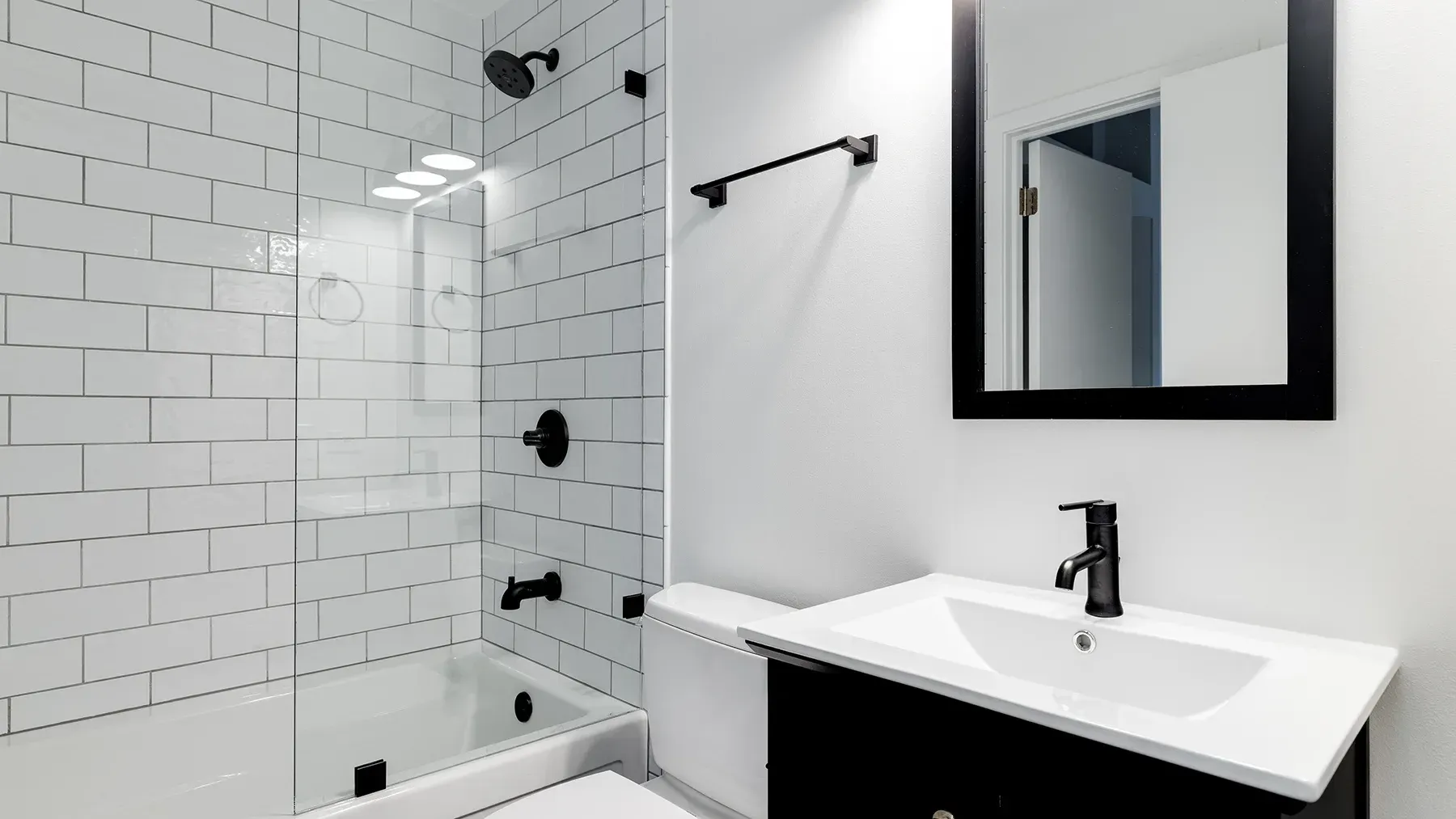 Modern white bathroom with subway tile shower, black fixtures, and a black vanity.