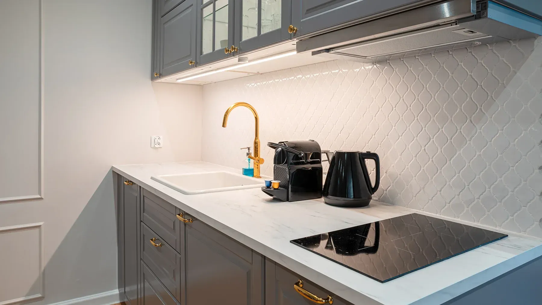 Gray and white kitchen with gold accents, including faucet and hardware. Black appliances sit on a white countertop.