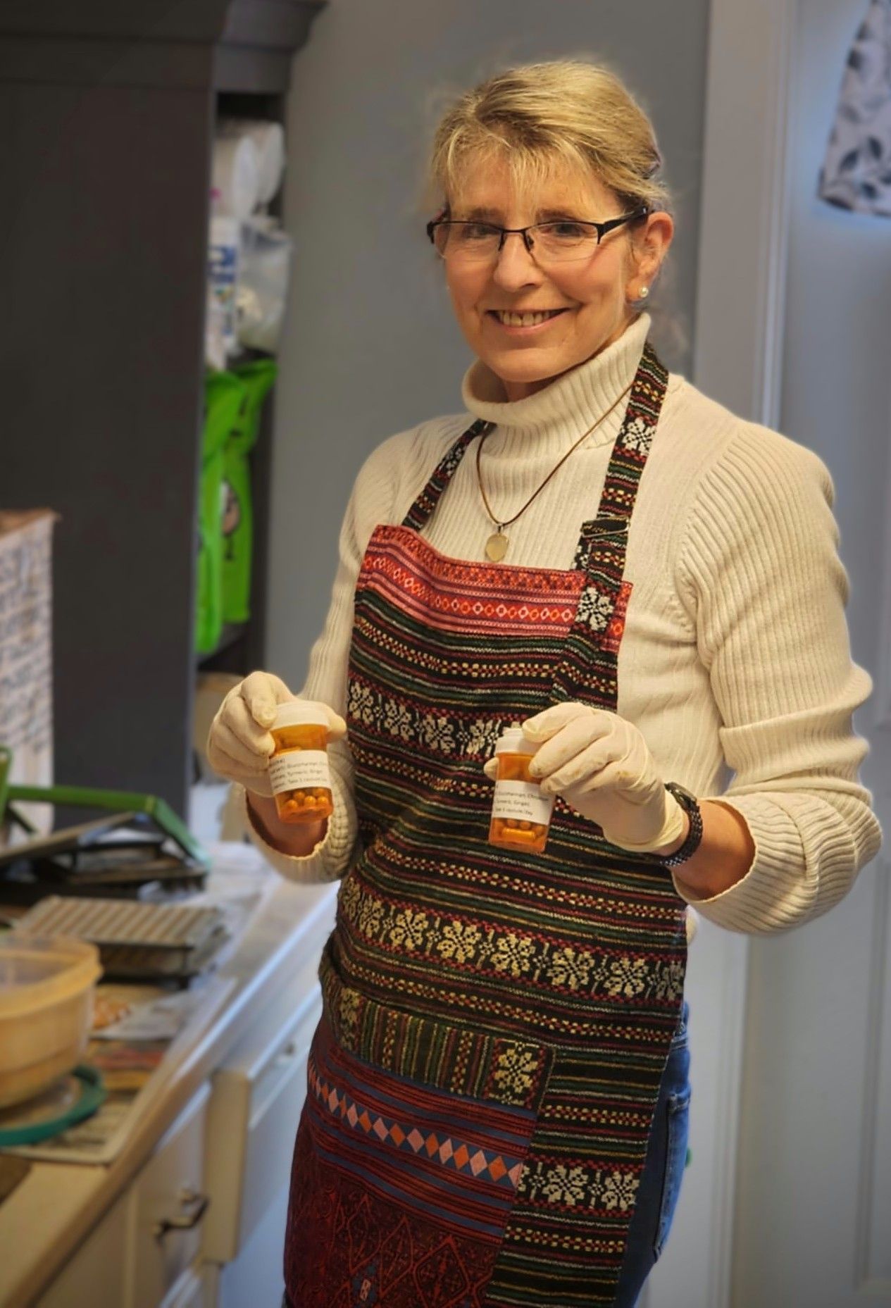 A woman in an apron is holding two small bottles of pills.