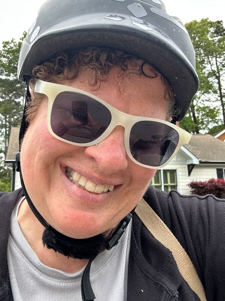 Founder of 404ebiketour, Anne Curtis, in white sunglasses and bike helmet, outdoors with houses and trees in the background
