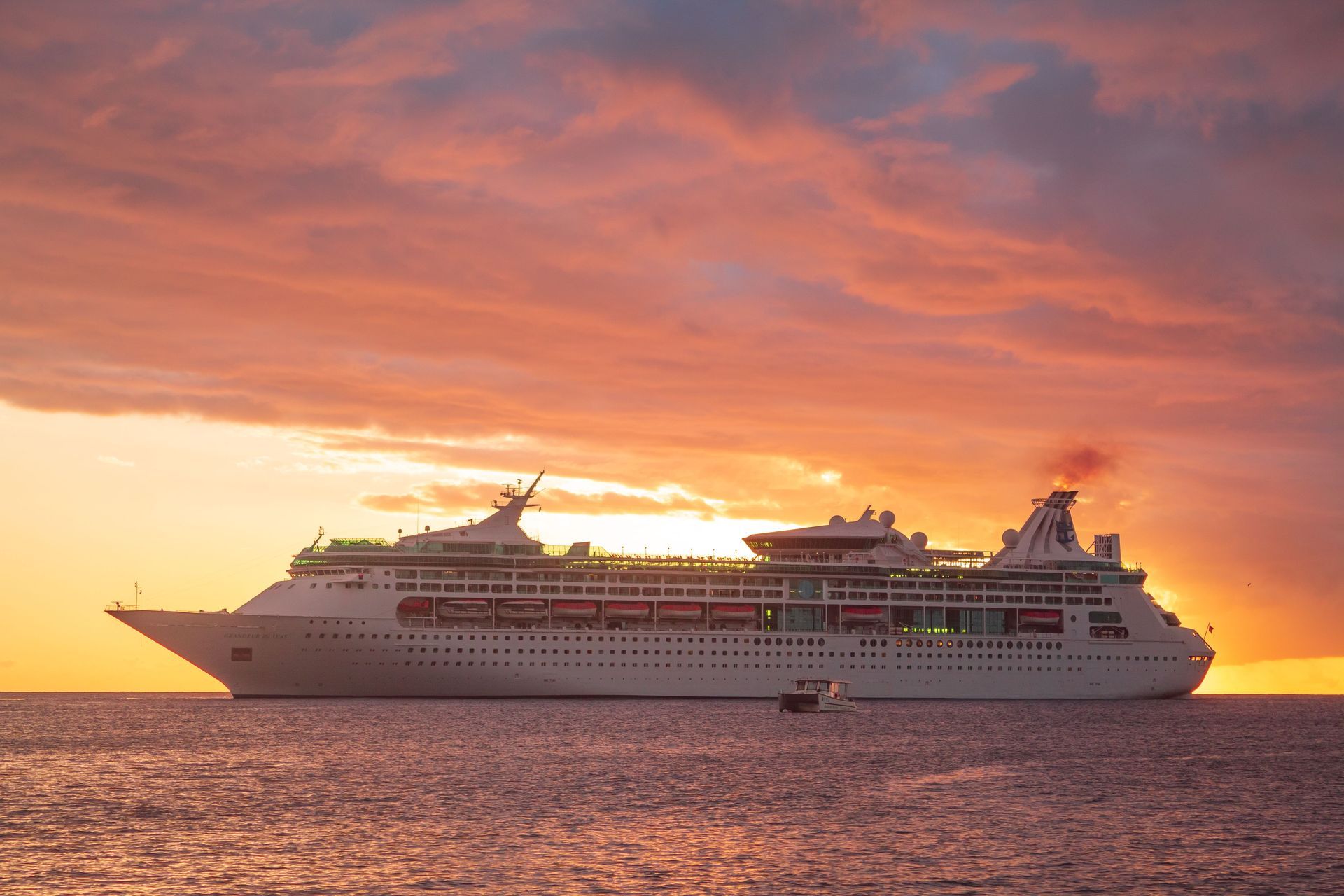 Cruise ship sailing at sunset on calm water under a pink-orange sky
