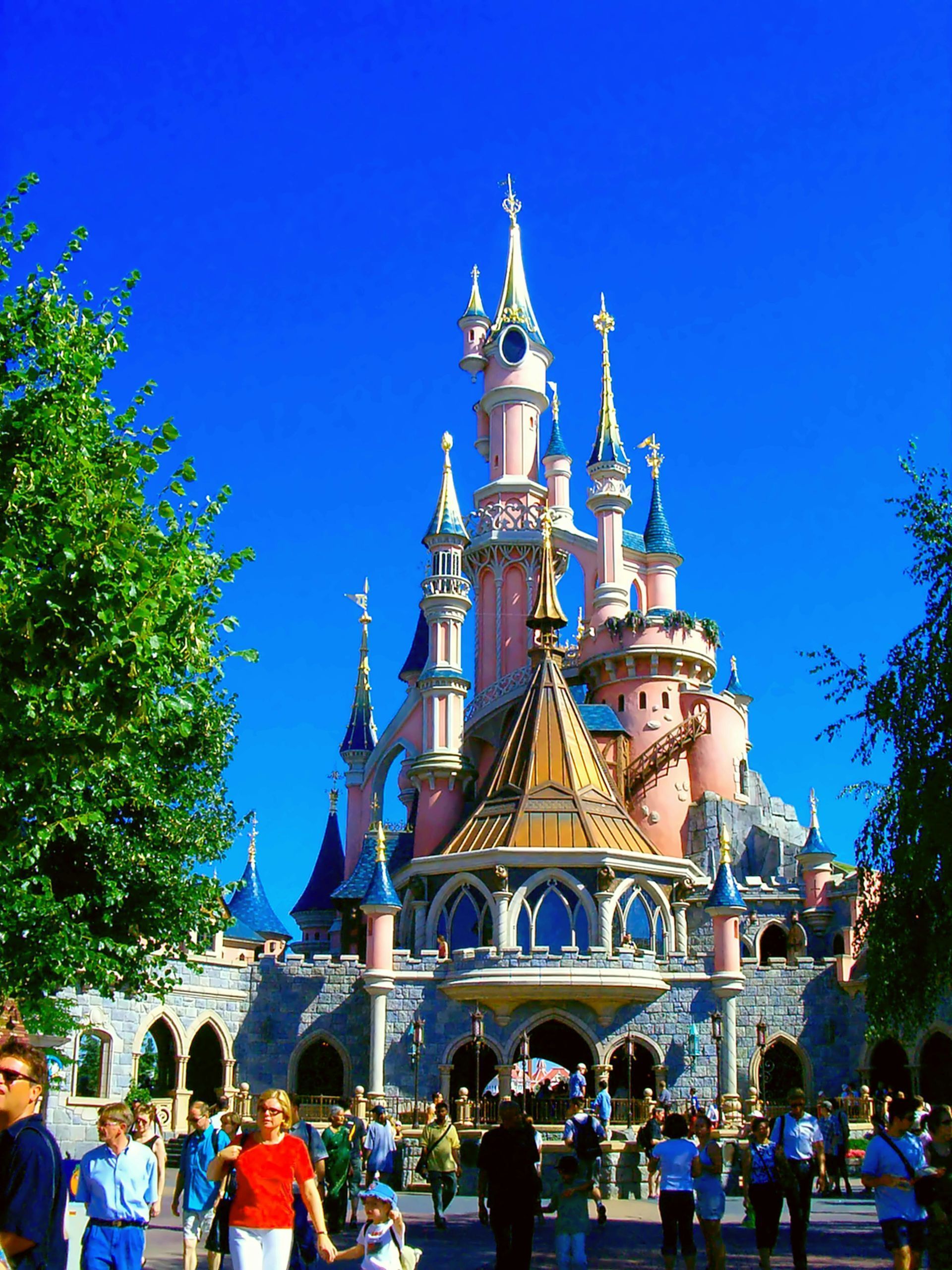Colorful castle at Disneyland with visitors in front under a bright blue sky