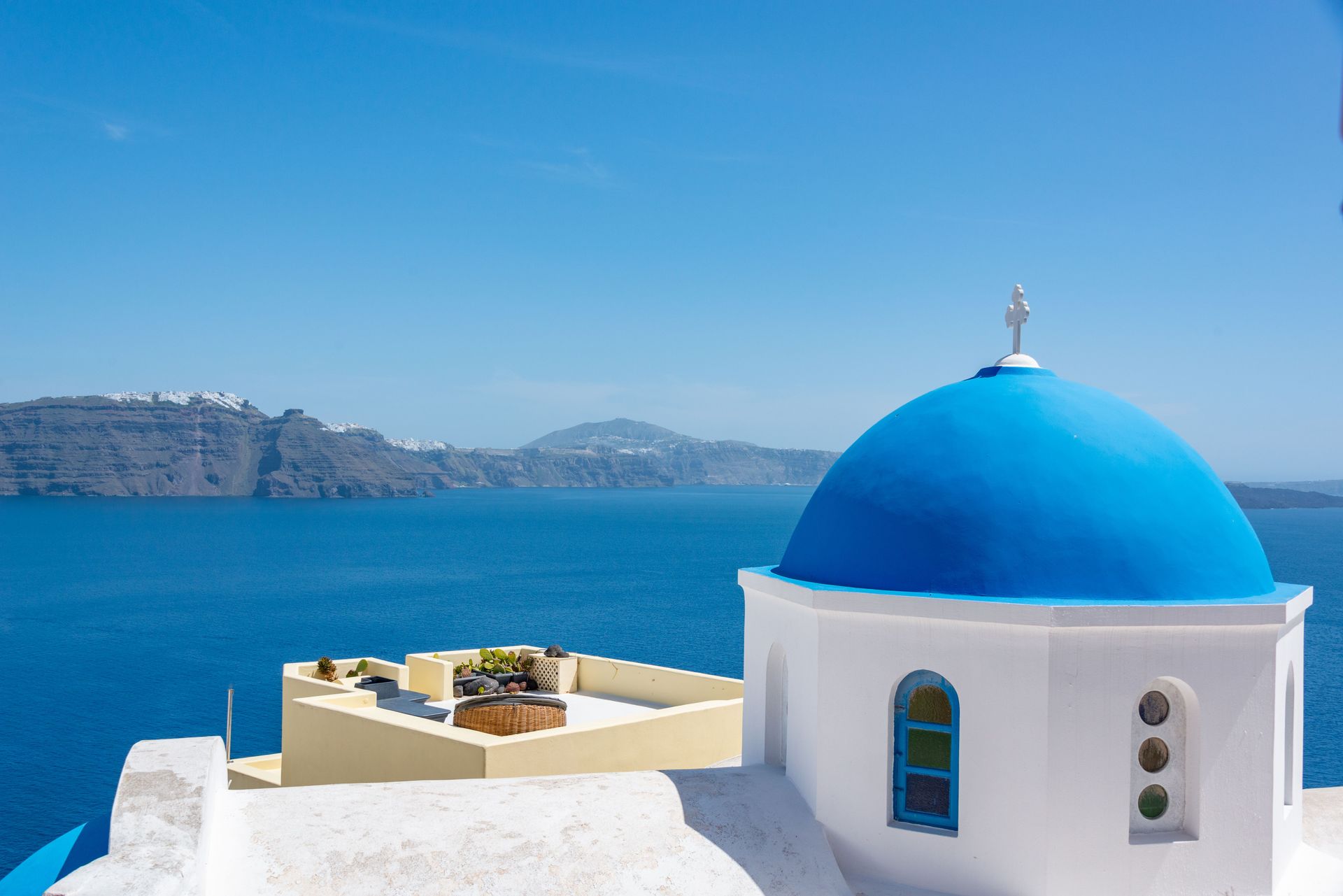 White-and-blue seaside building with a domed roof overlooking a bright blue sea and distant cliffs.