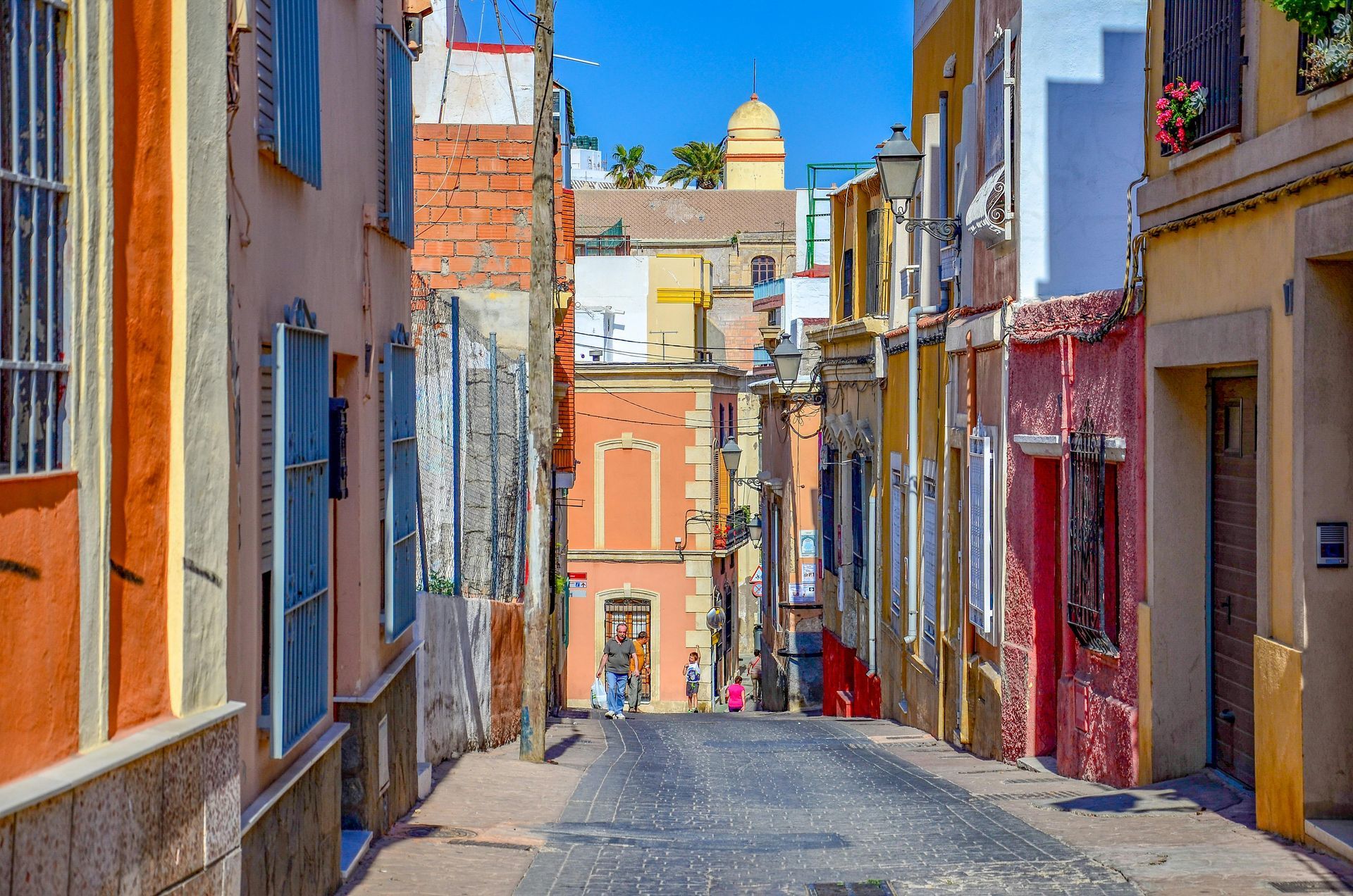 Colorful narrow street with tall buildings and a distant domed tower under a bright blue sky