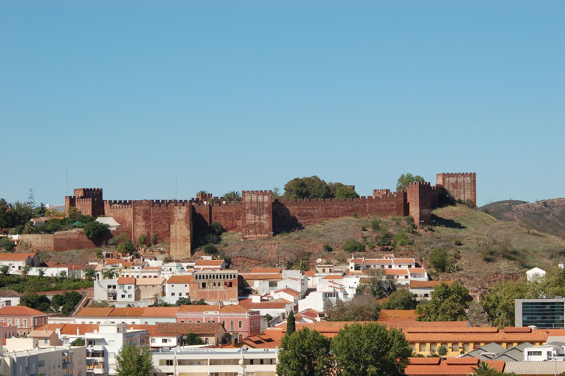 Stone fortress walls on a hill above a white-roofed town under a clear blue sky