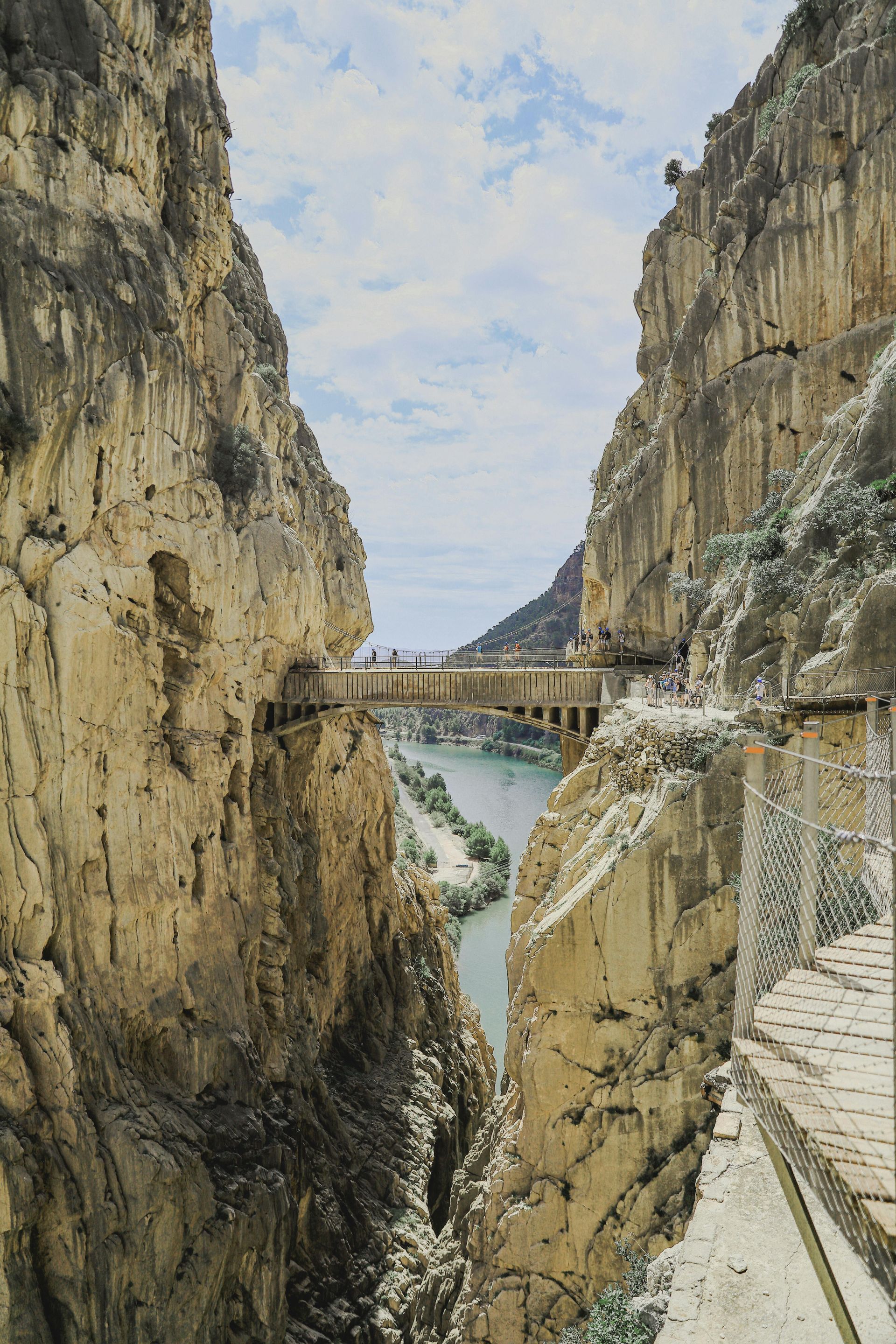 Narrow canyon with a river, stone bridge, and wooden walkway along the cliffside