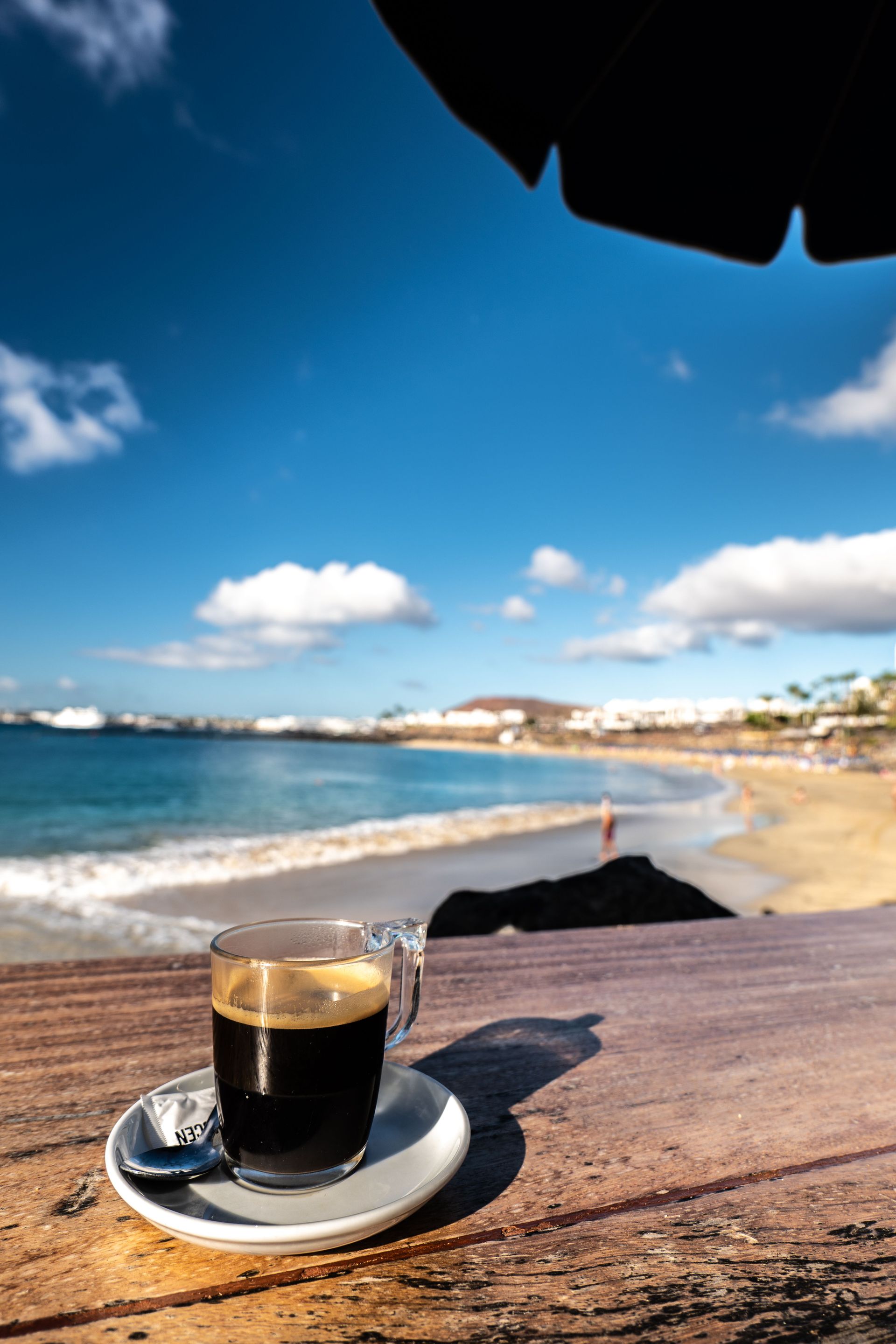 Coffee on a saucer on a wooden table by a sunny beach and blue ocean
