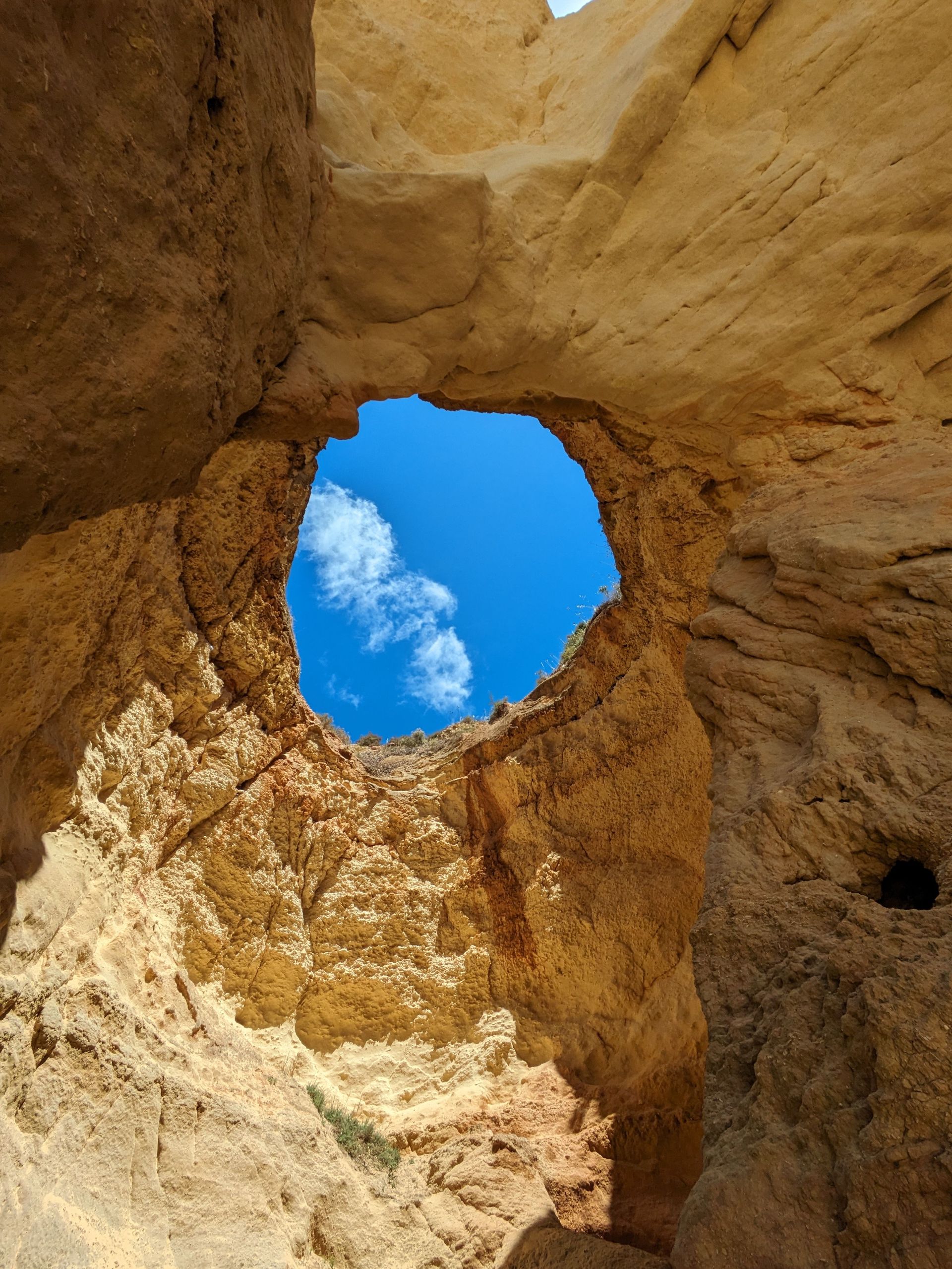 Rocky canyon walls framing a round opening of blue sky and clouds