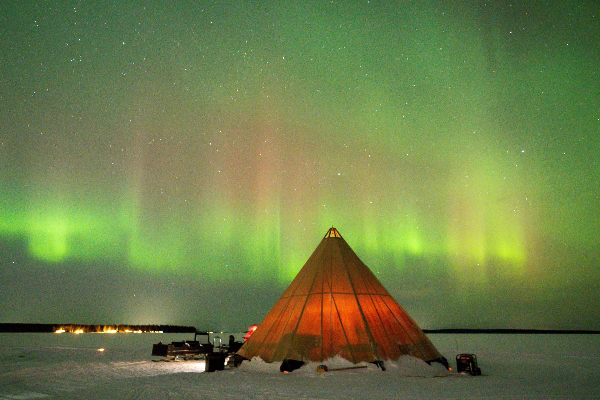Snowy teepee under green and pink aurora borealis in a dark night sky