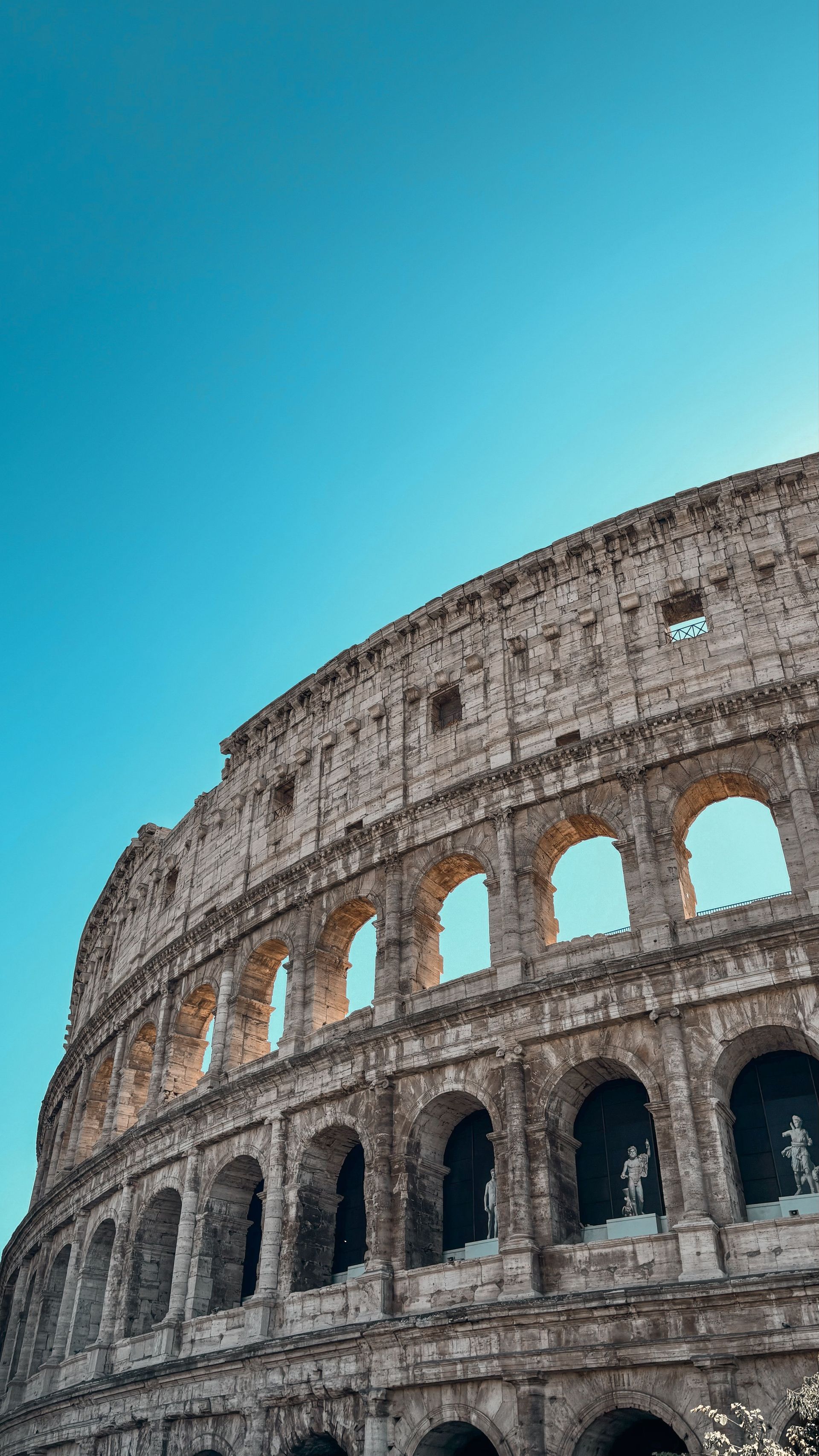 Low-angle view of the Colosseum against a bright blue sky
