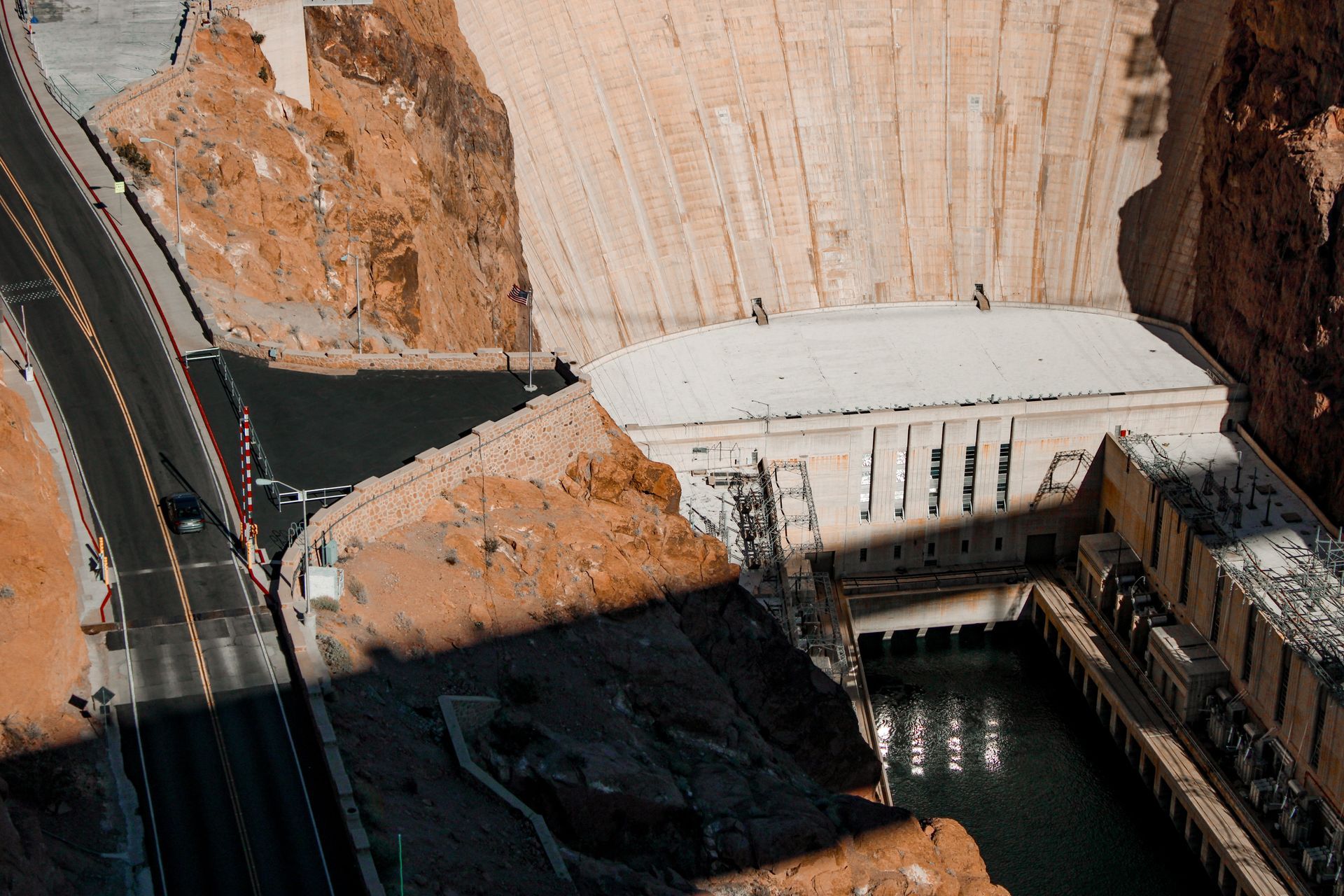 Aerial view of a large dam with a spillway, reservoir, and road along the canyon edge.