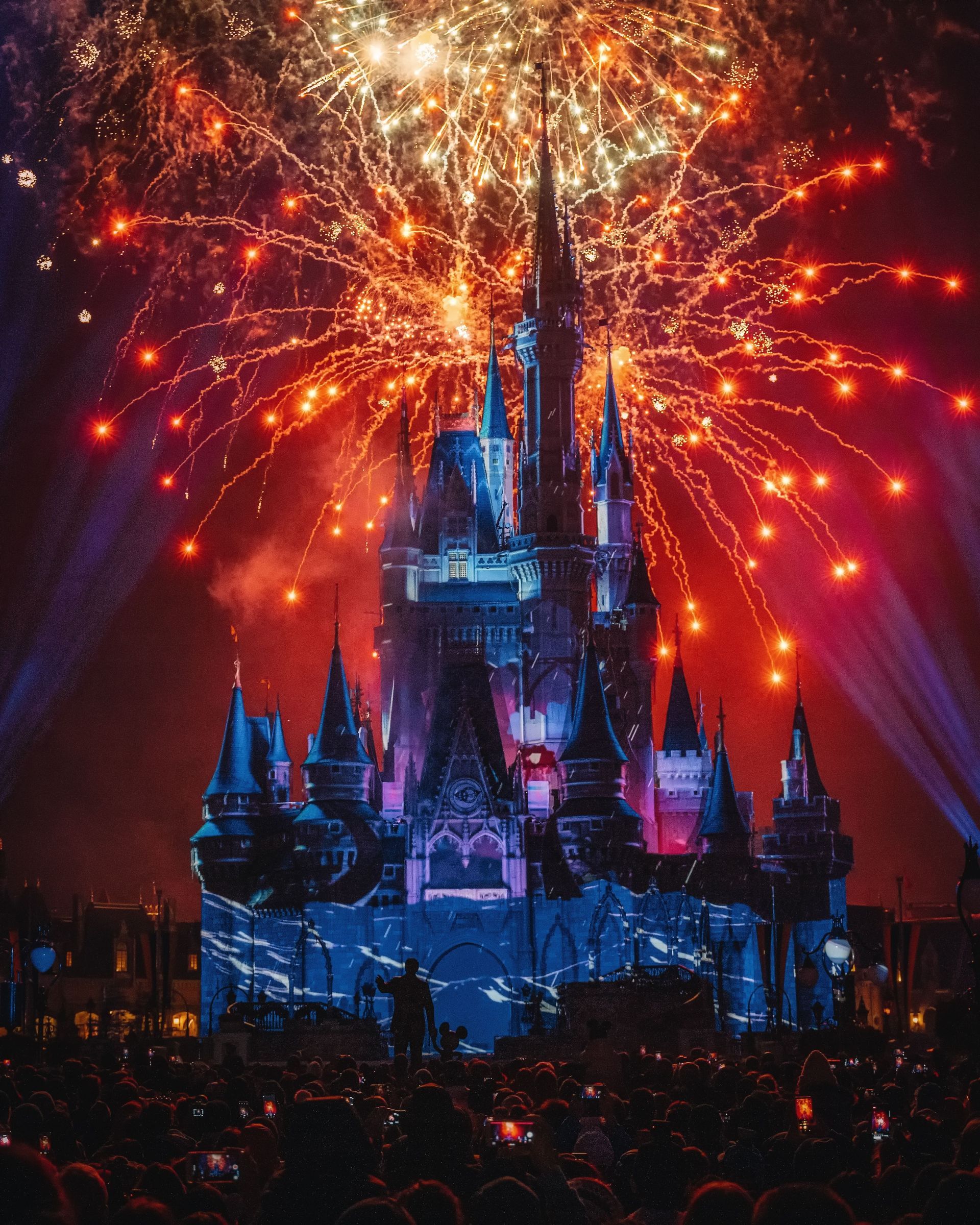 Fireworks bursting above a lit-up fairy-tale castle at night