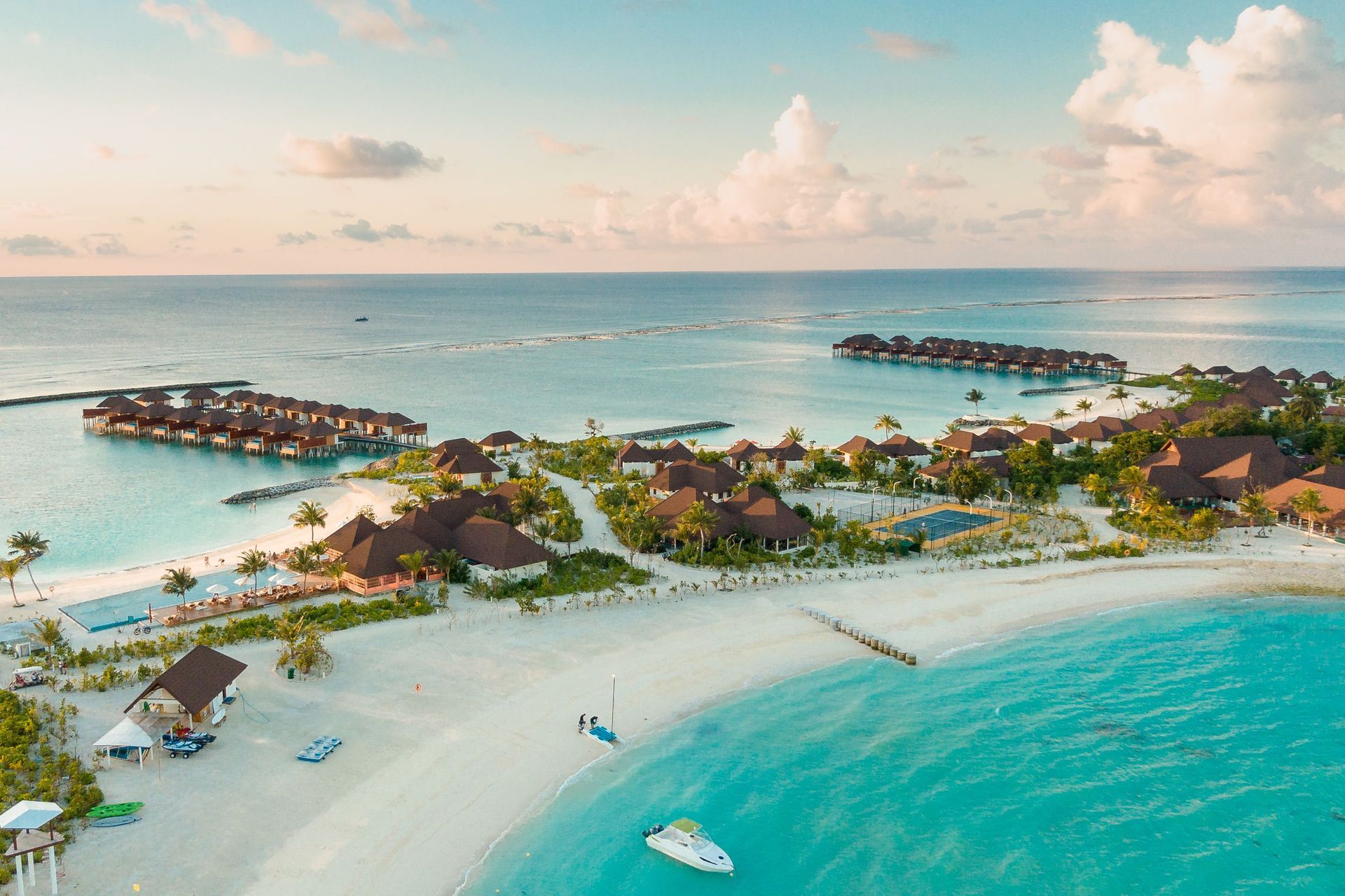 Aerial view of a tropical island resort with white sand beaches, turquoise water, and overwater bungalows