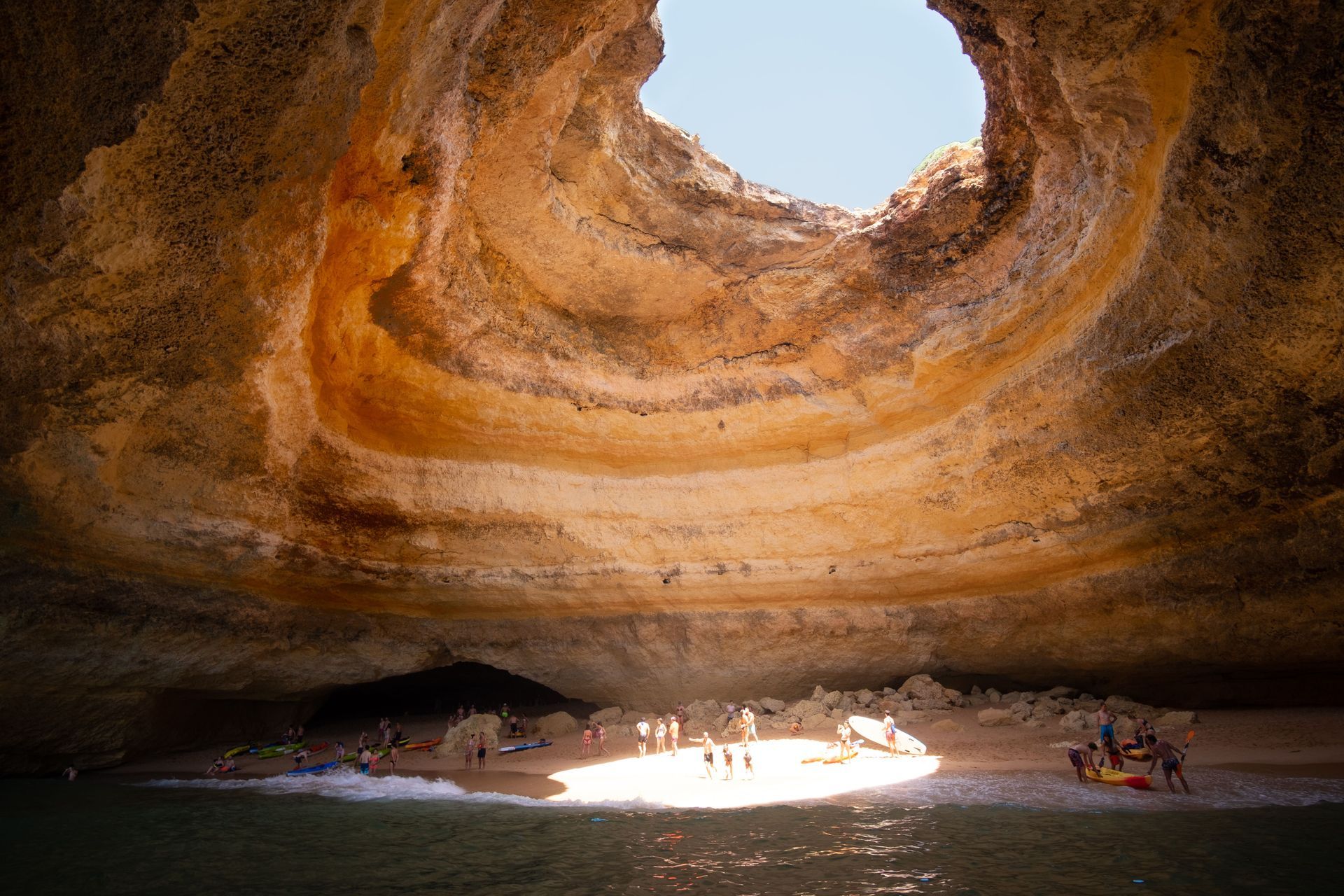 People in a sunlit sea cave with a large circular opening in the rocky ceiling
