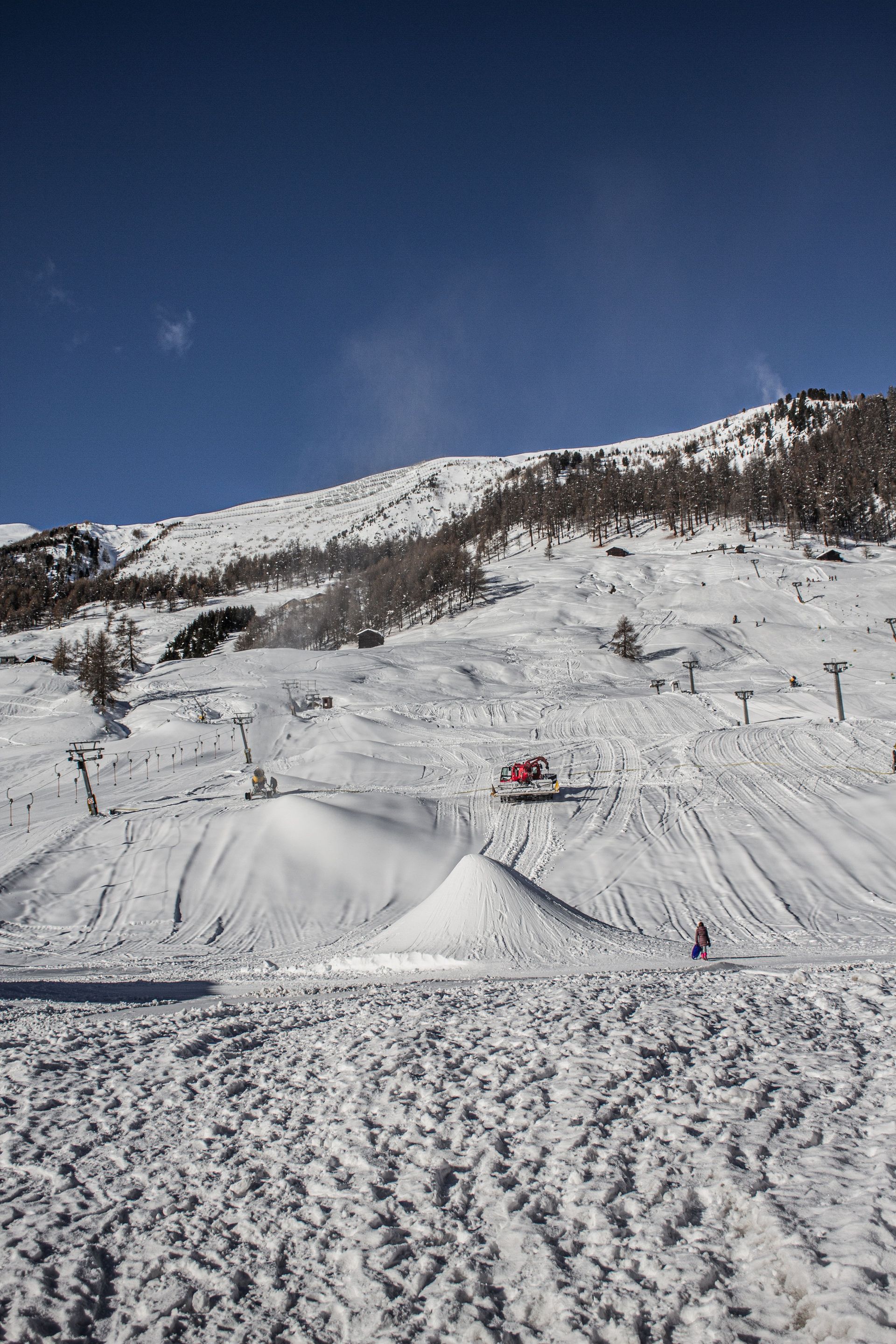 Snowy ski slope with a small skier in red under a clear blue sky