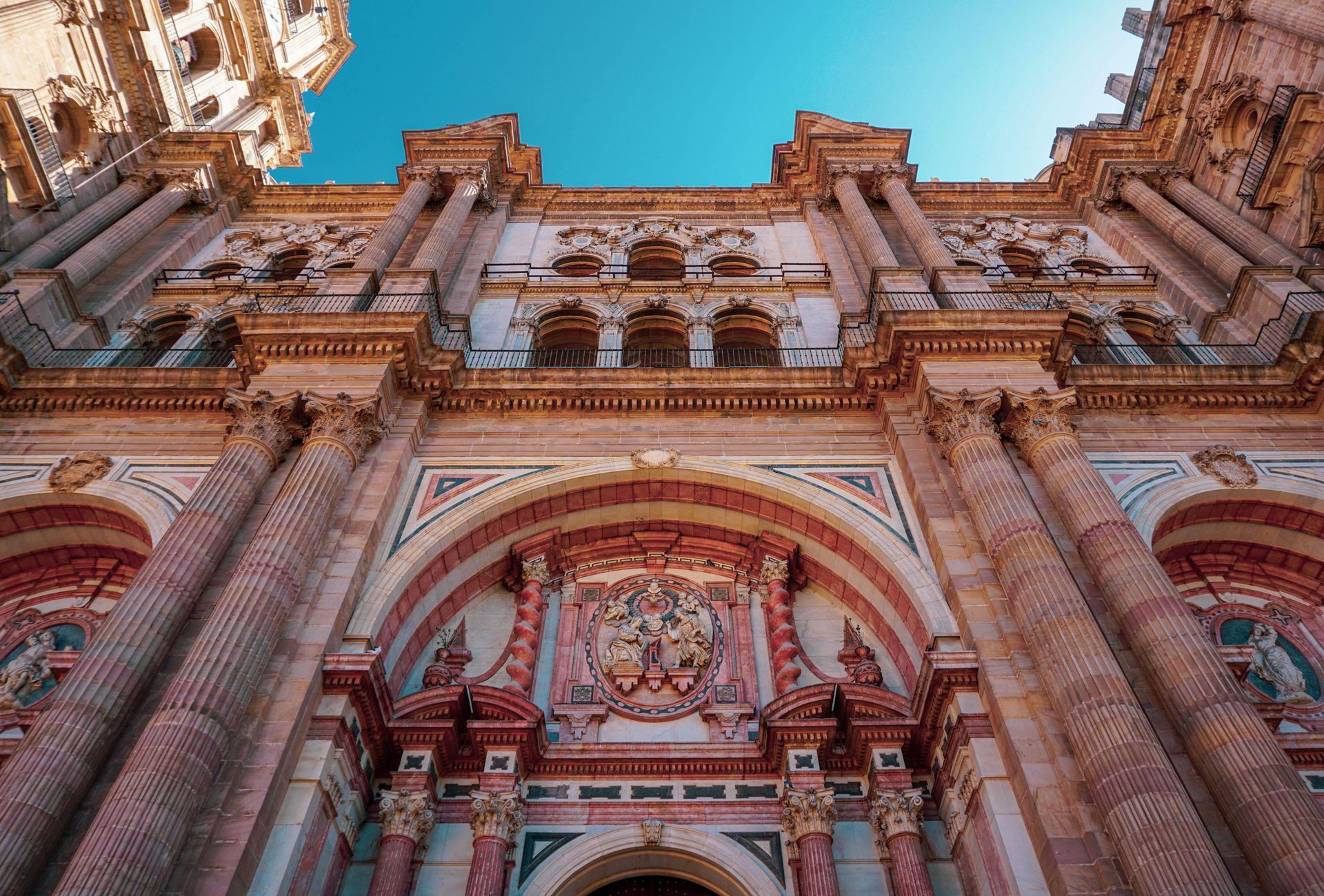 Ornate red stone cathedral facade with arched entrance and blue sky overhead