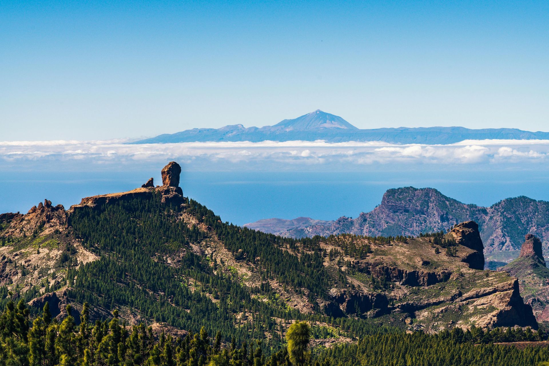 Mountain landscape with rocky peaks, green hills, and a distant blue sea under a clear sky