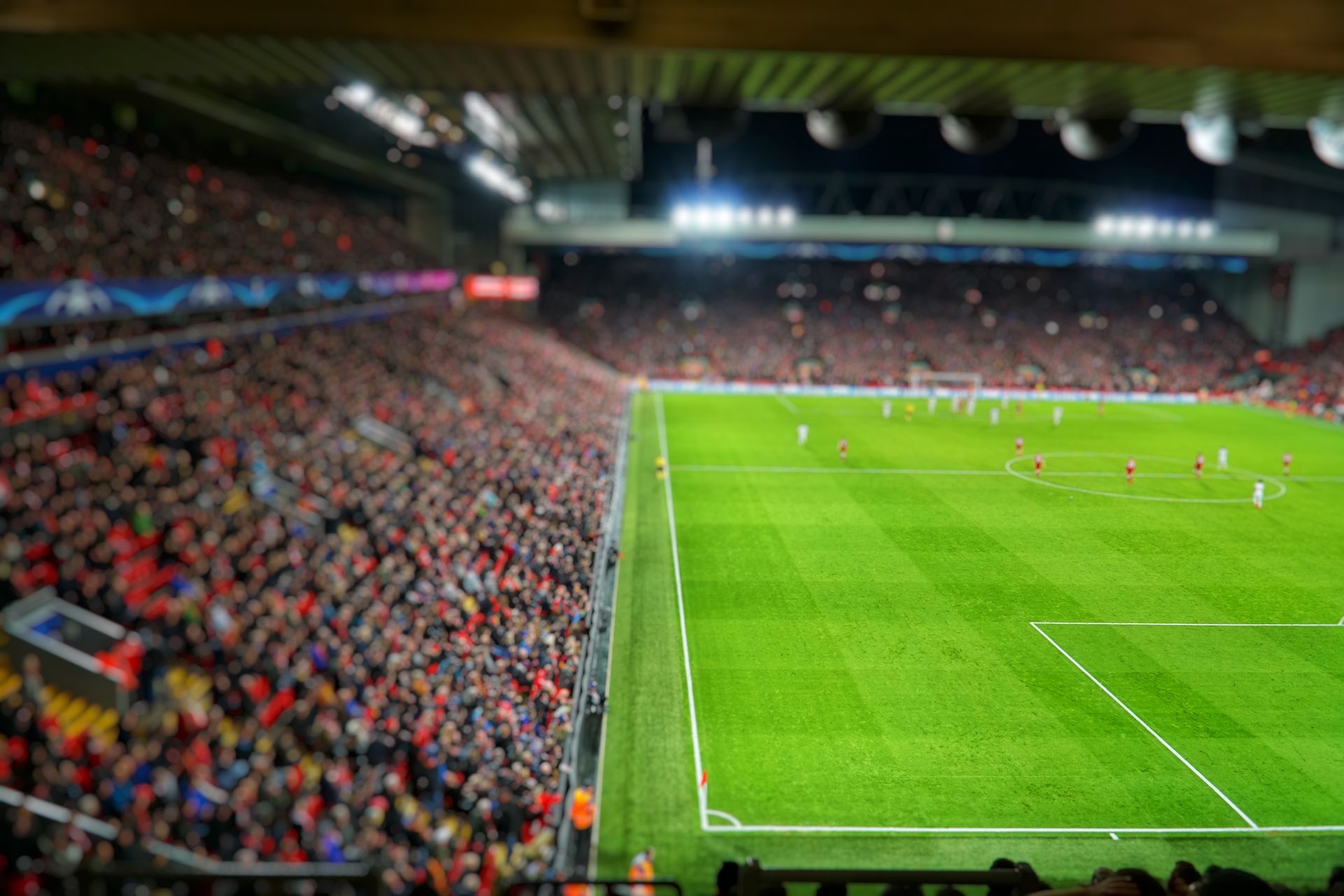 Packed soccer stadium with a green pitch and players under bright lights