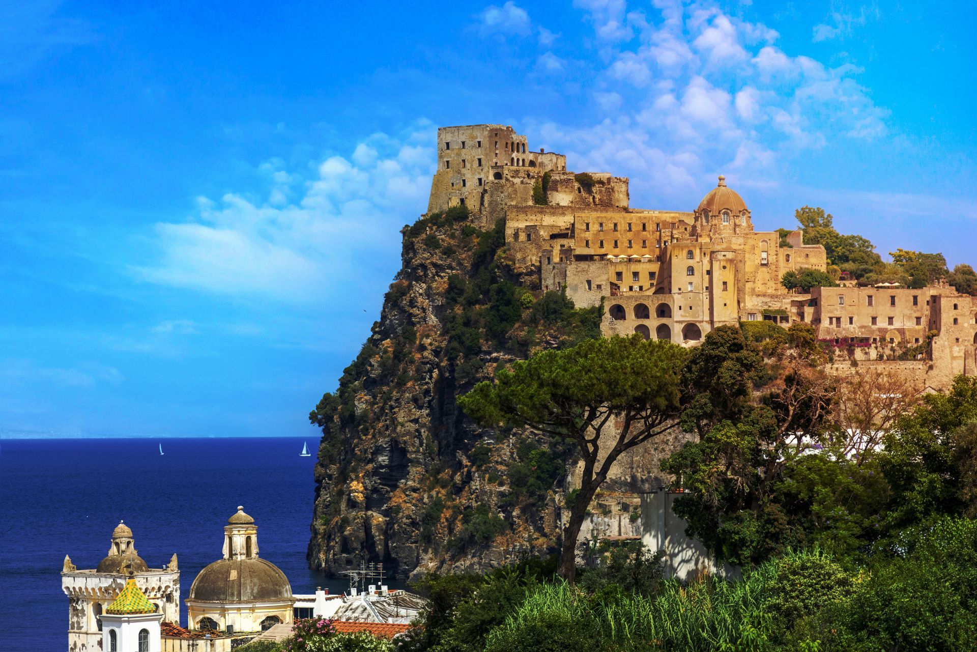 Cliffside village on a rocky promontory above the sea, with blue sky and church domes below