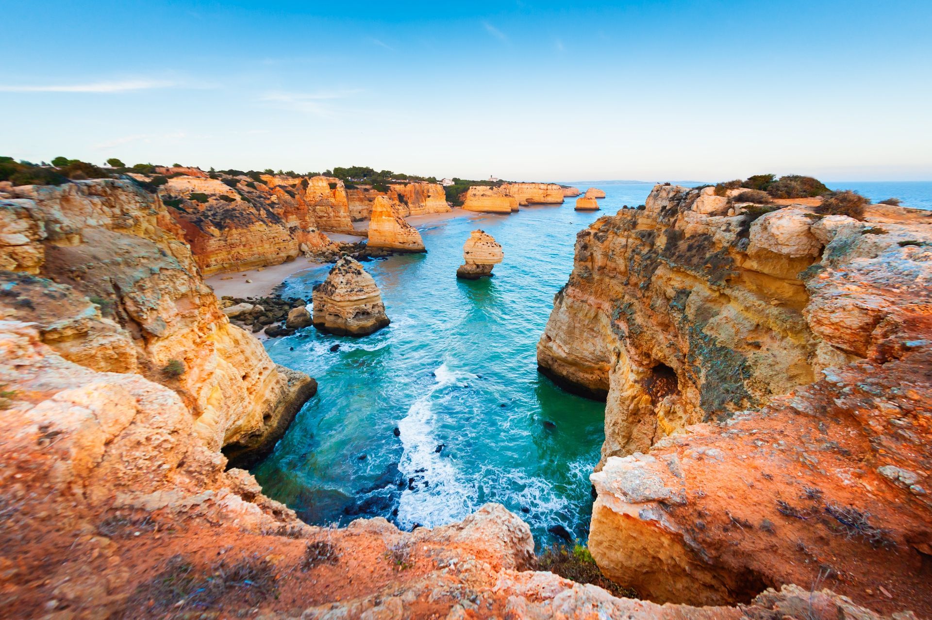 Rocky coastal cove with turquoise water and orange cliffs under a clear sky
