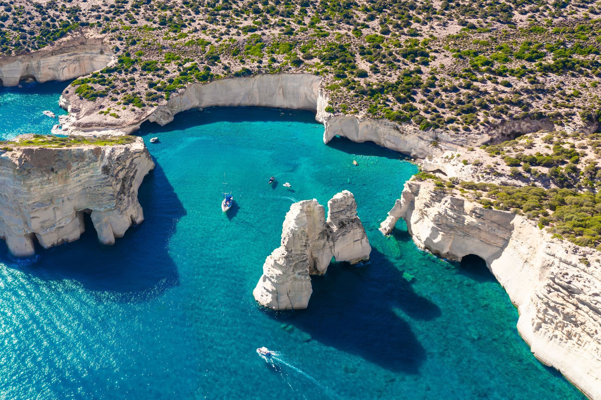 Turquoise cove with white cliffs, rock formations, and a small boat on clear blue water