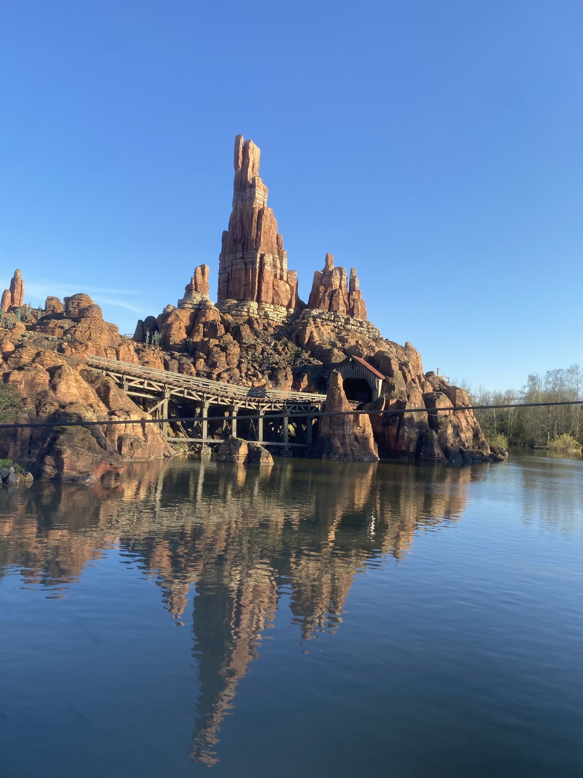 Rocky spire and cliffs reflected in a calm lake under a clear blue sky.