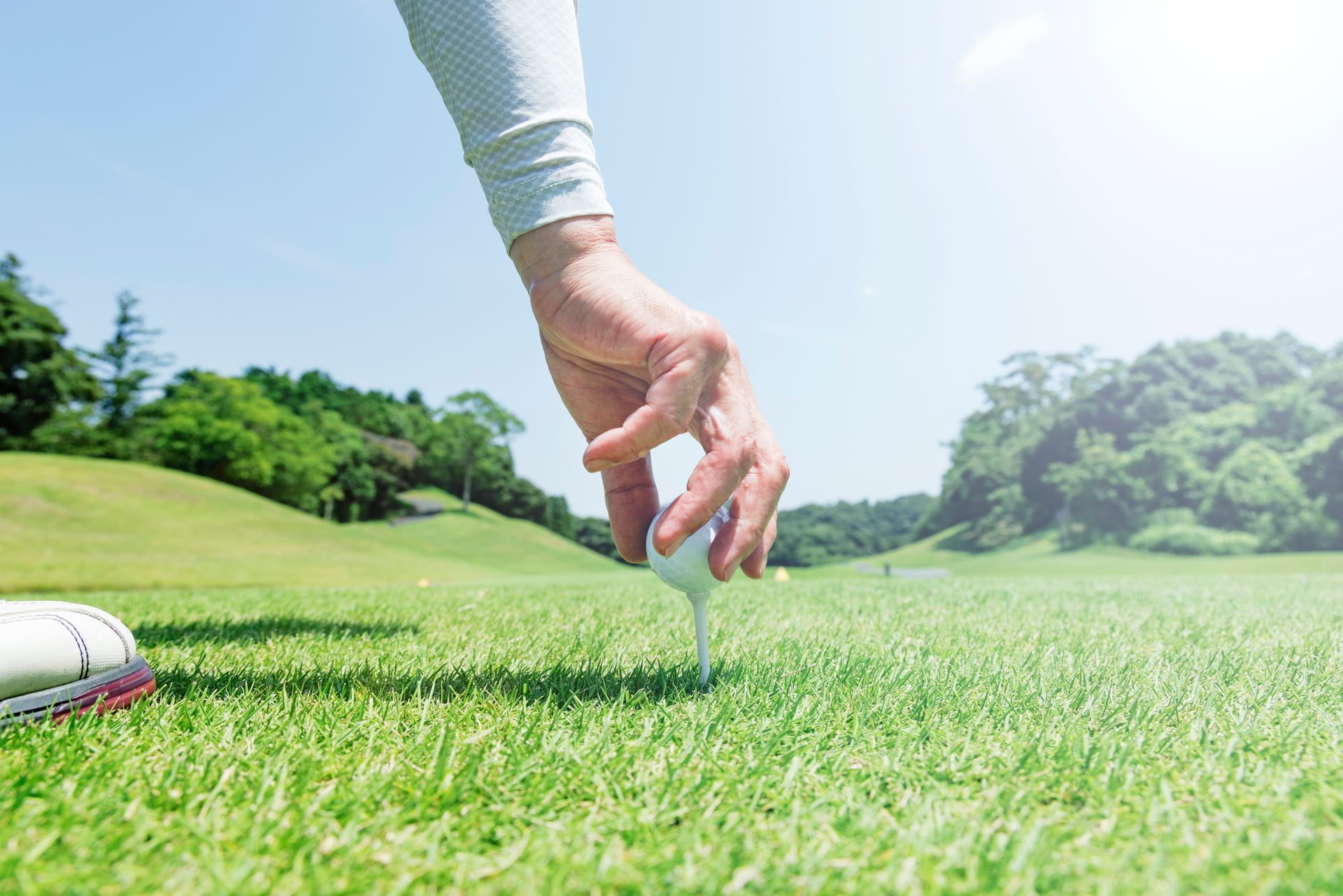 Golfer placing a tee on a green course under bright sunlight