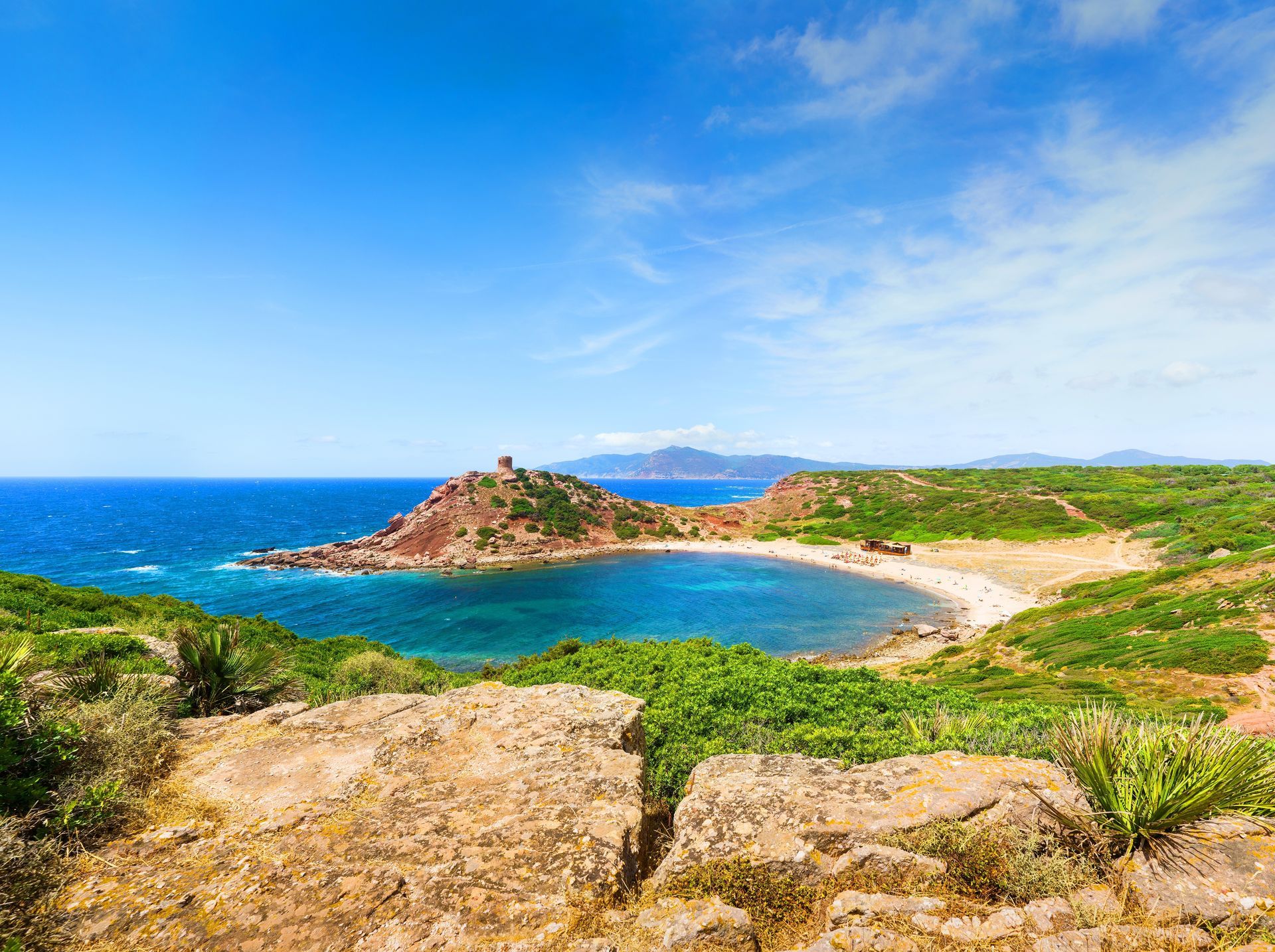 Rocky coastline with a turquoise bay, sandy beach, and blue sky