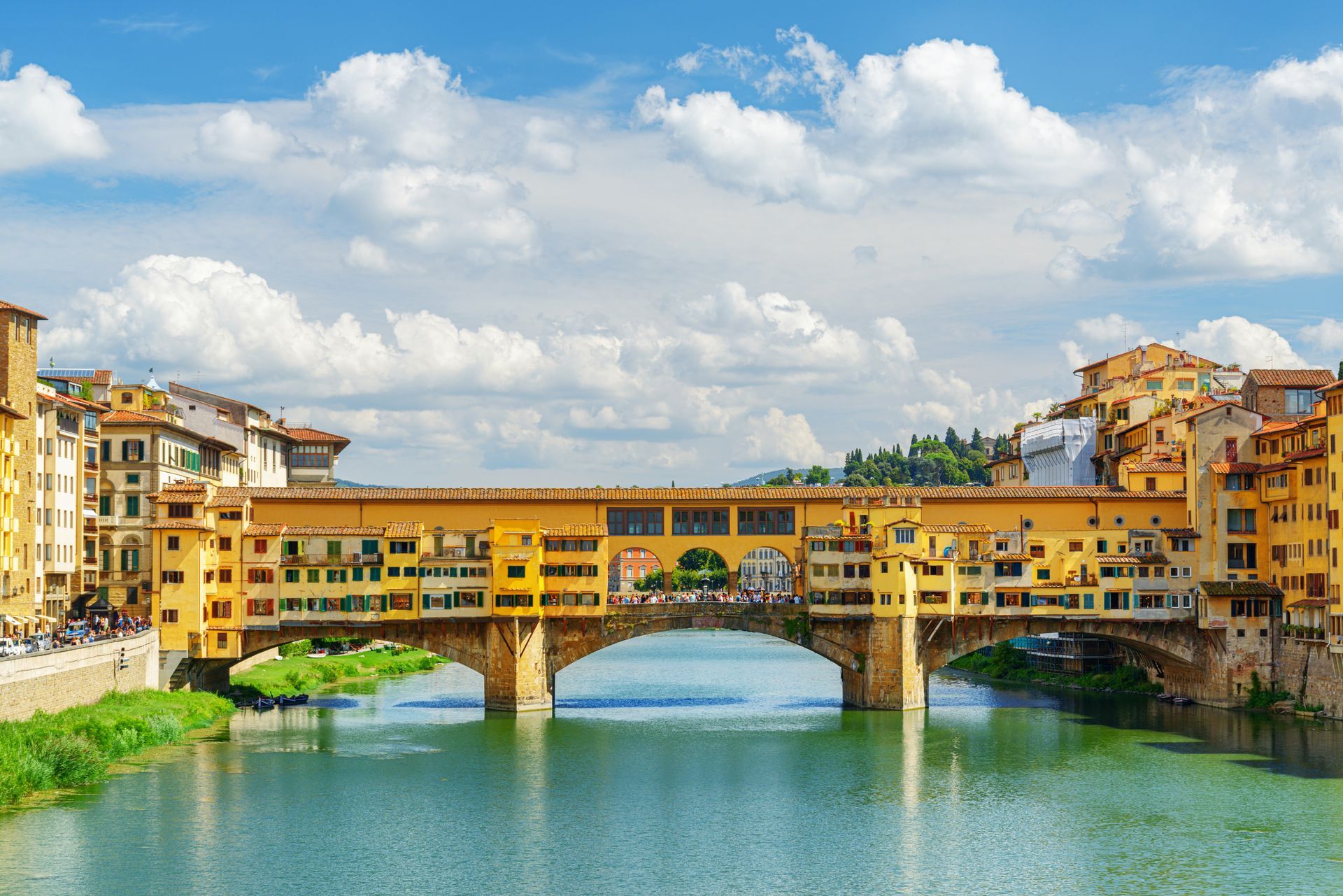 Historic bridge over a river in Florence with yellow buildings under a blue sky