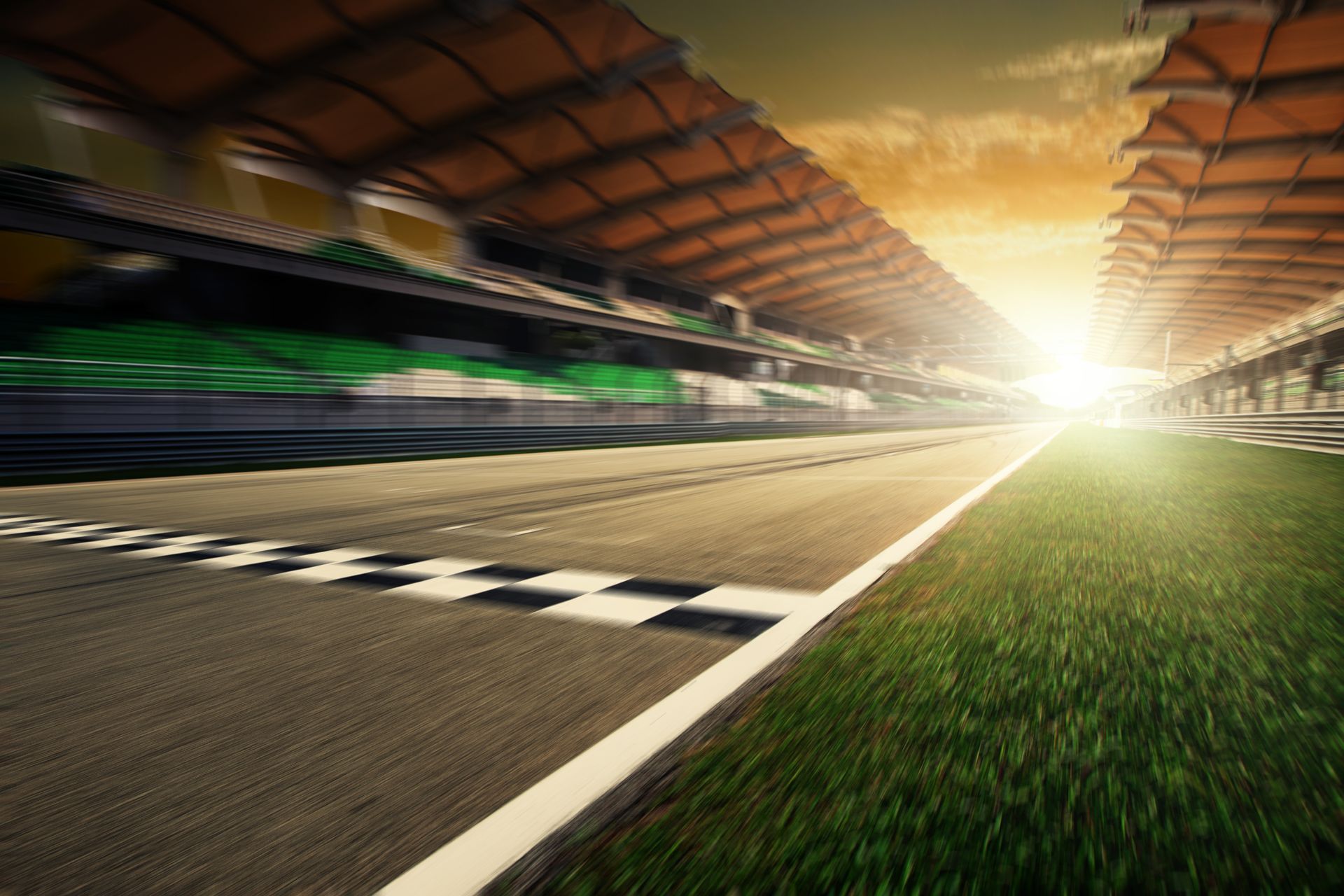 Empty racetrack at sunset with blurred cars speeding past the starting line and grandstands overhead