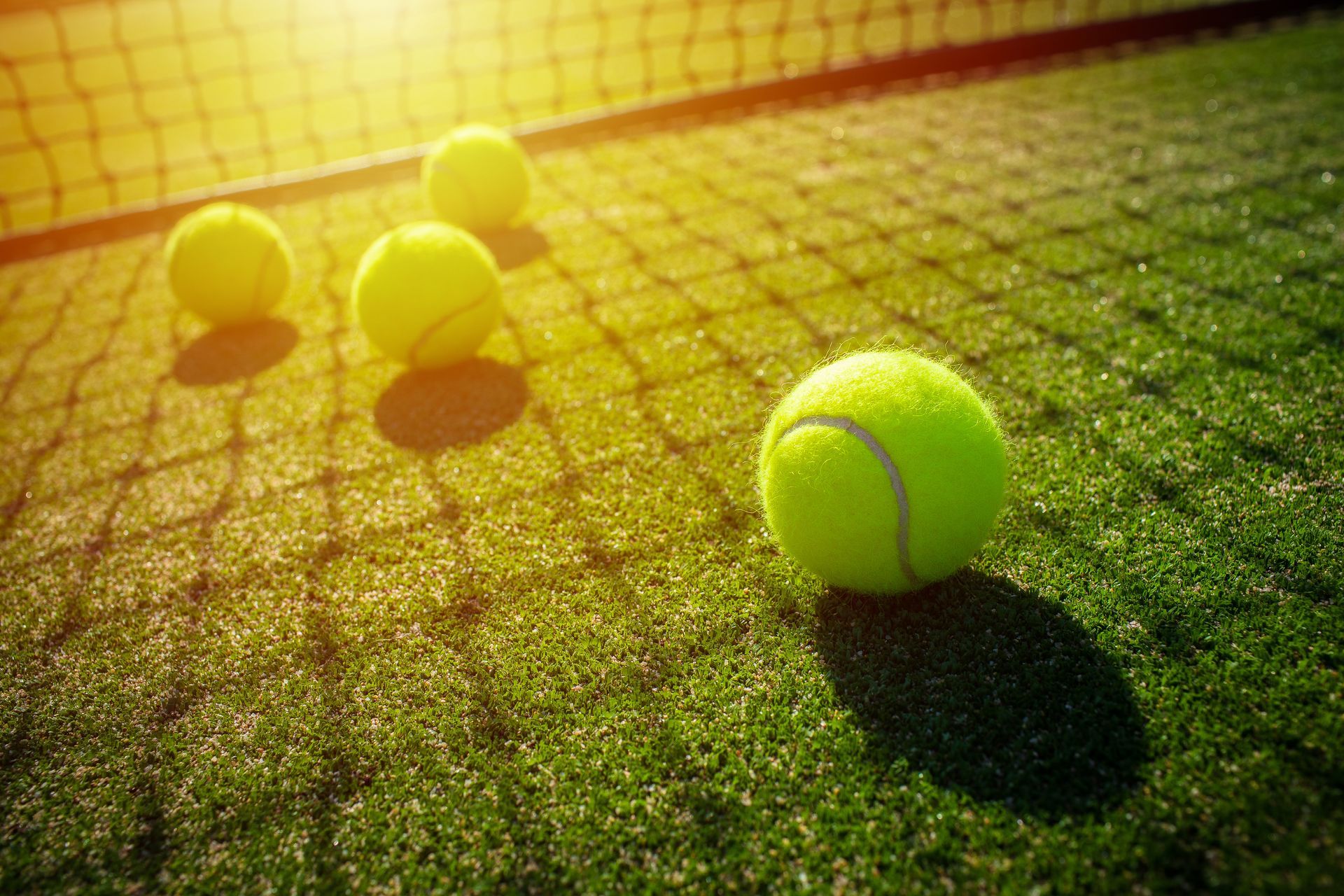 Three tennis balls on a sunlit court, with one ball in sharp focus in the foreground