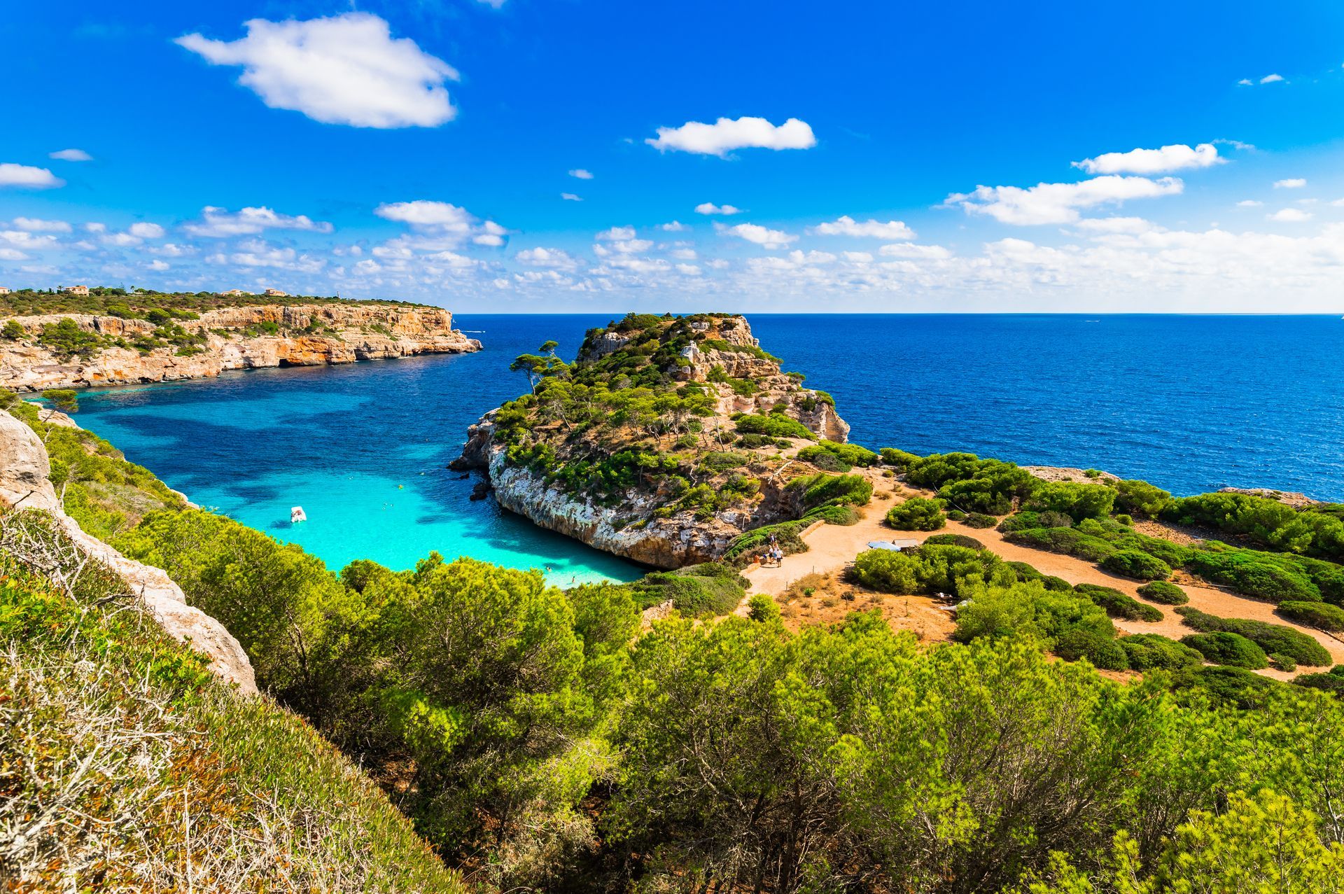 Bright turquoise cove with rocky cliffs, green shrubs, and a deep blue sea under a sunny sky