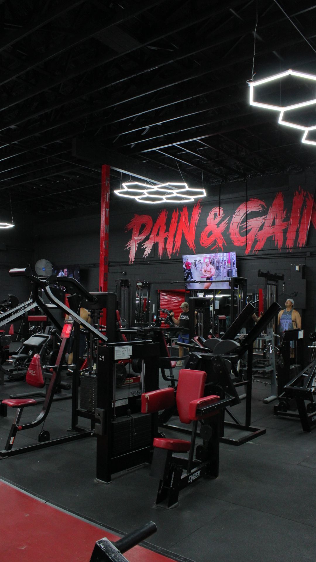 Modern gym interior with red and black equipment and a neon “PAIN & GAIN” sign