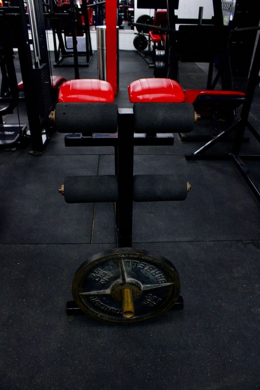 Gym equipment with red pads and a weight plate on the floor in a dark fitness room