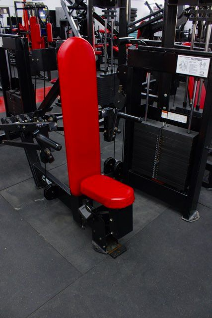 Red padded gym machine seat with tall backrest in a fitness equipment showroom