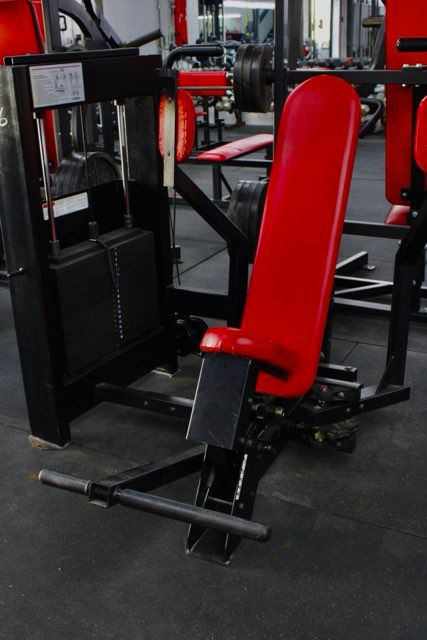 Red gym workout machine with padded seat and black frame in a fitness room