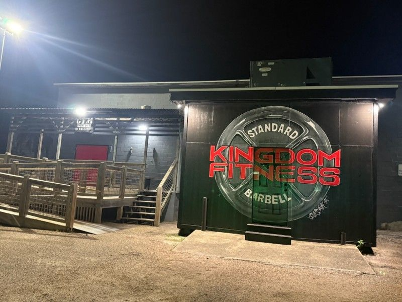 Kingdom Fitness sign on a dark building at night, with outdoor stairs and a lit entrance.