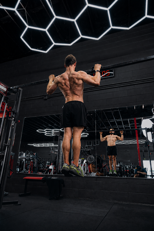 Man doing pull-ups in a gym with mirrored walls and hexagon ceiling lights