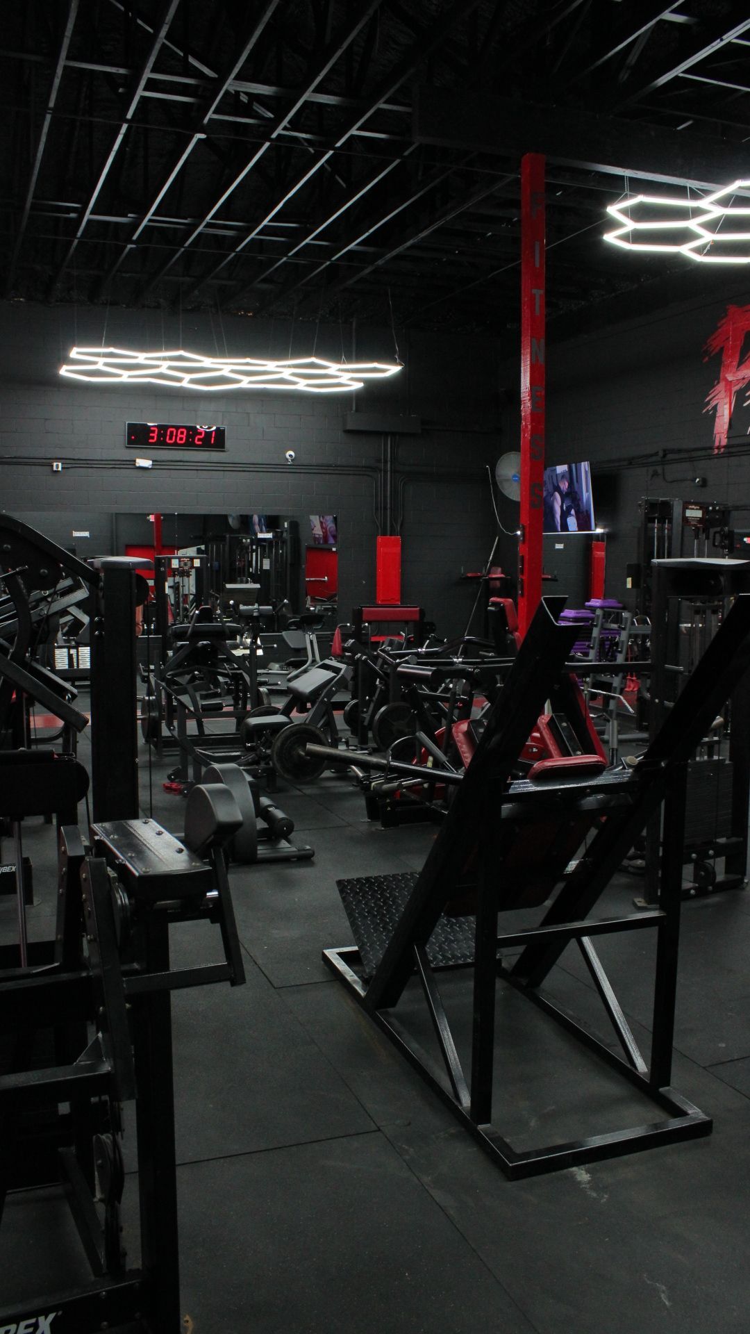 Dimly lit gym interior with black and red equipment, including weight machines and a squat rack.