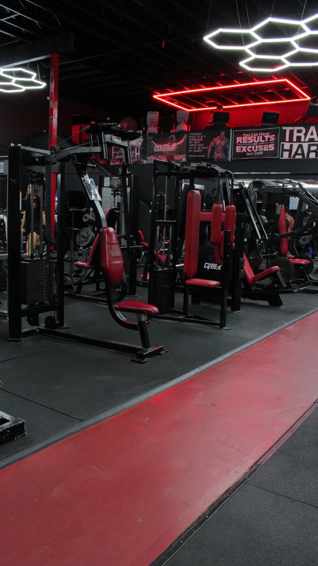 Empty gym with black and red exercise machines and hexagonal ceiling lights.