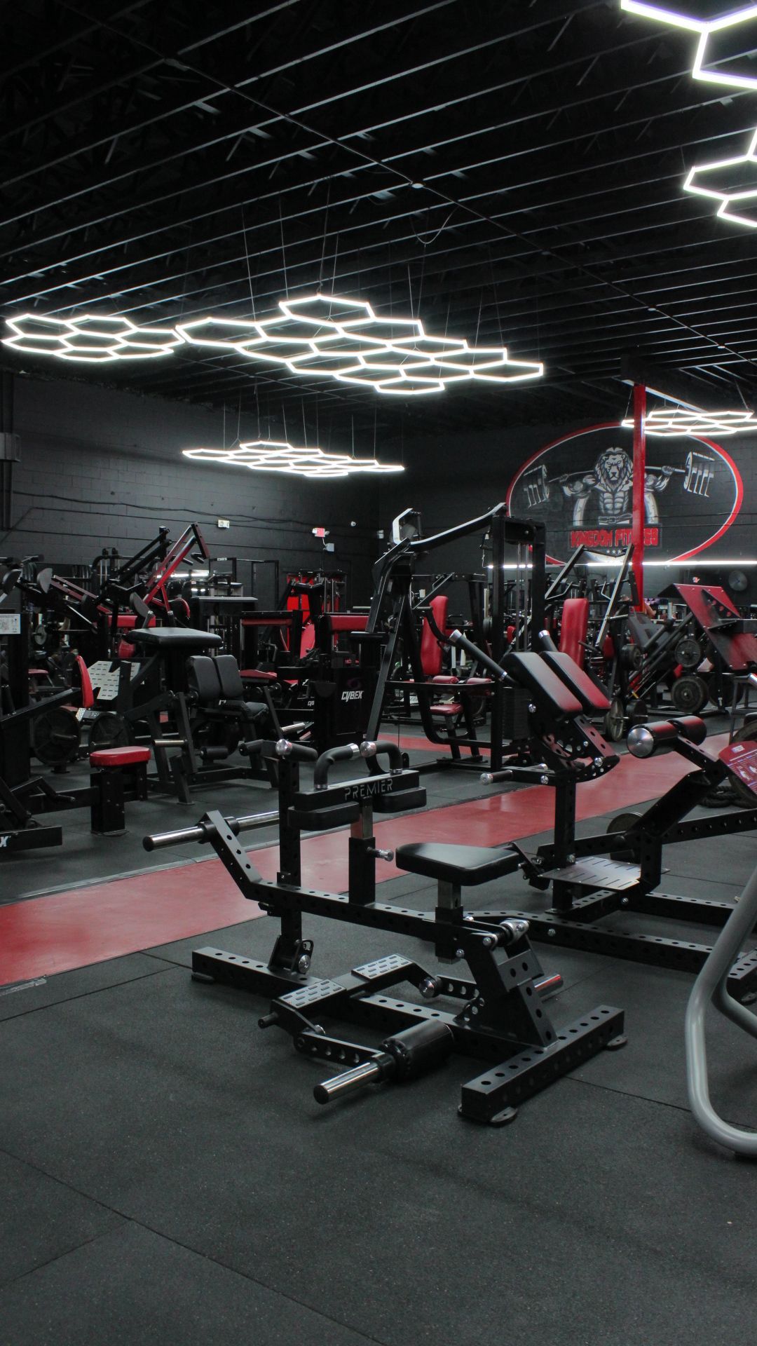 Empty modern gym with black and red equipment under geometric ceiling lights.