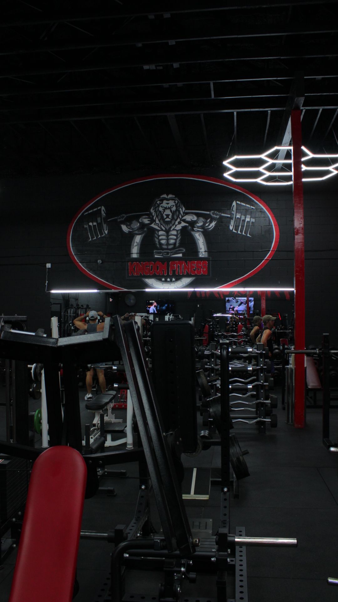 Dark gym interior with red accents, exercise machines, and a large neon sign on the wall
